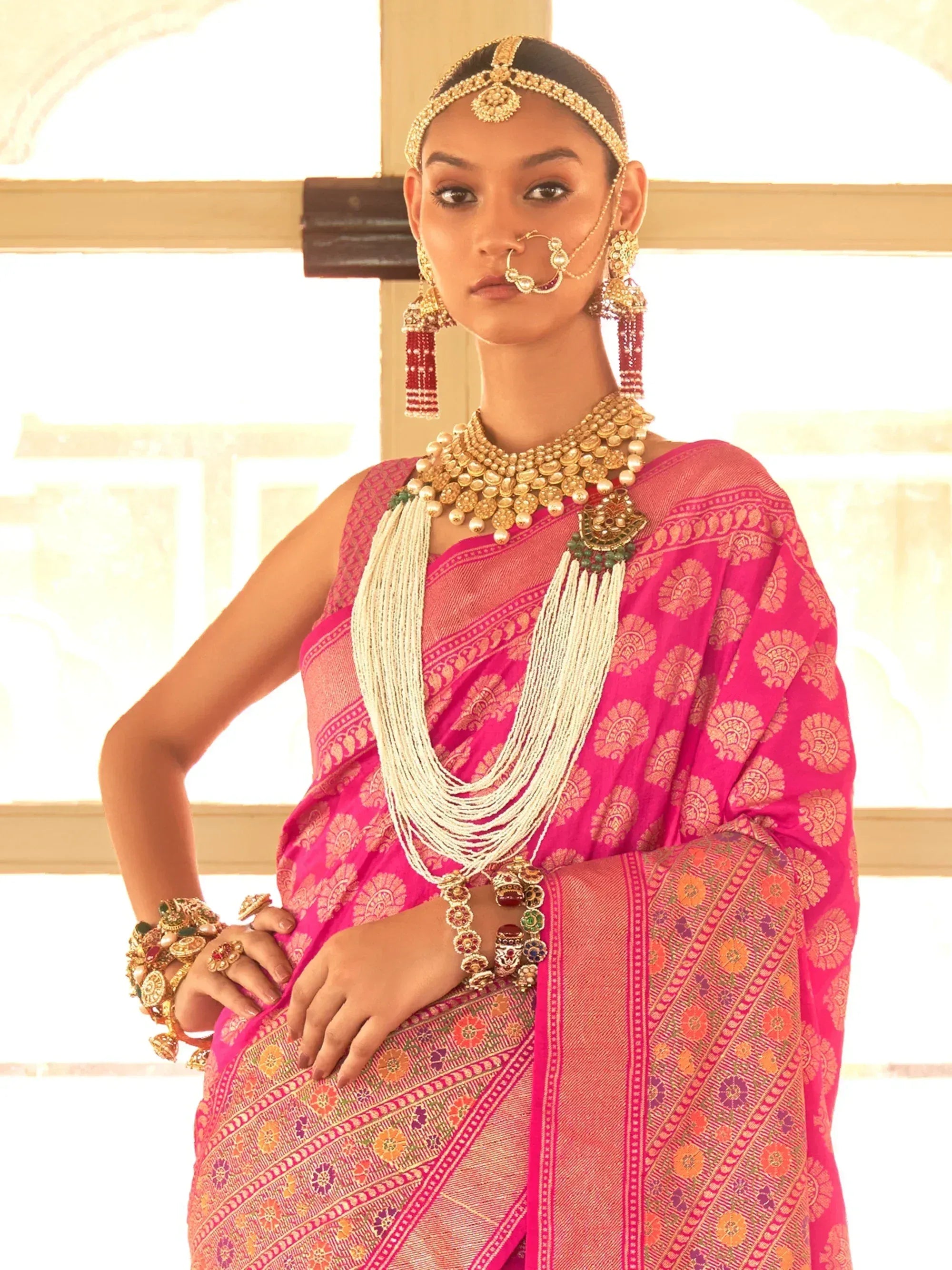 Woman in vibrant pink ethnic saree with gold jewelry and traditional Indian bridal accessories