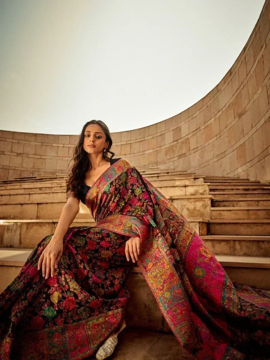 Woman in vibrant floral designer saree with rich border, seated on stone steps
