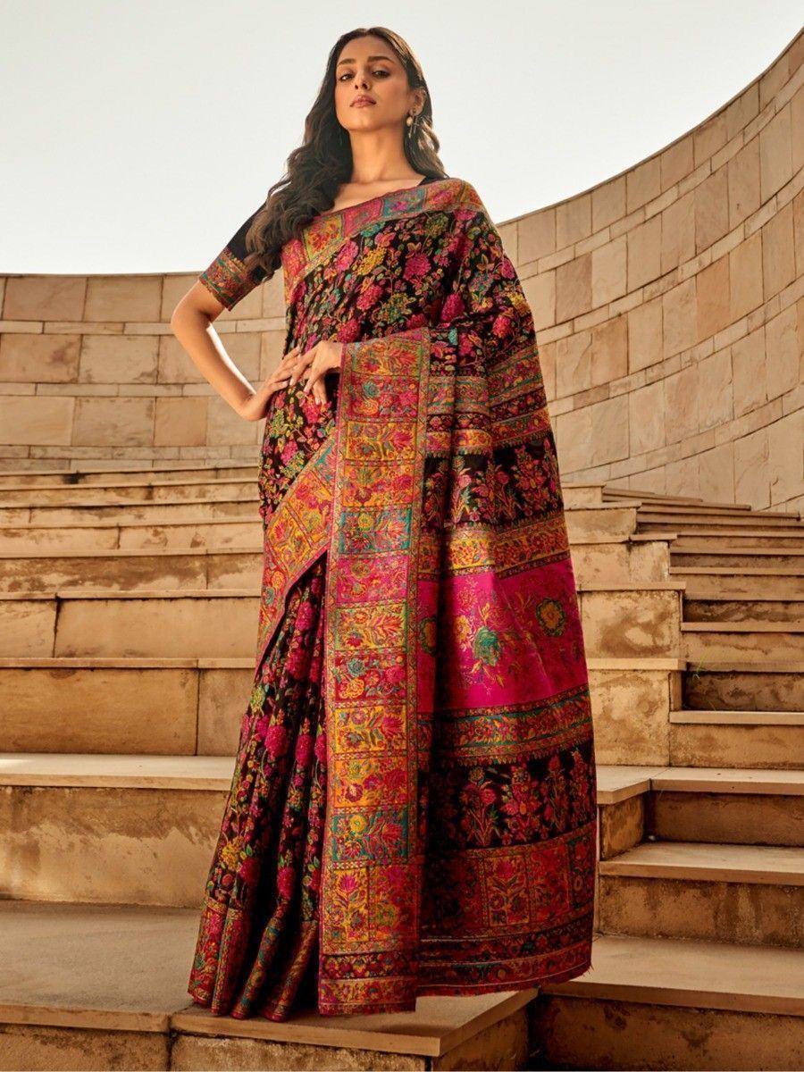 Woman in vibrant floral saree with intricate border, standing on stone steps