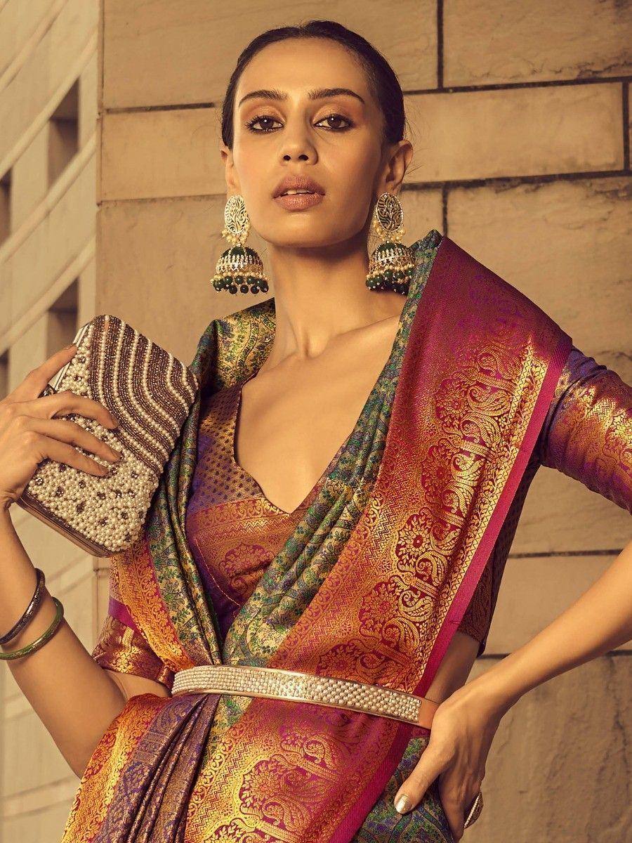 Woman in vibrant Indian saree with gold embroidery, jhumka earrings, and beaded clutch, styled for festive occasions.