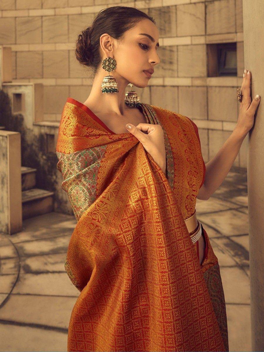 Woman in elegant orange and red designer saree with intricate patterns, traditional jhumka earrings, and ethnic styling