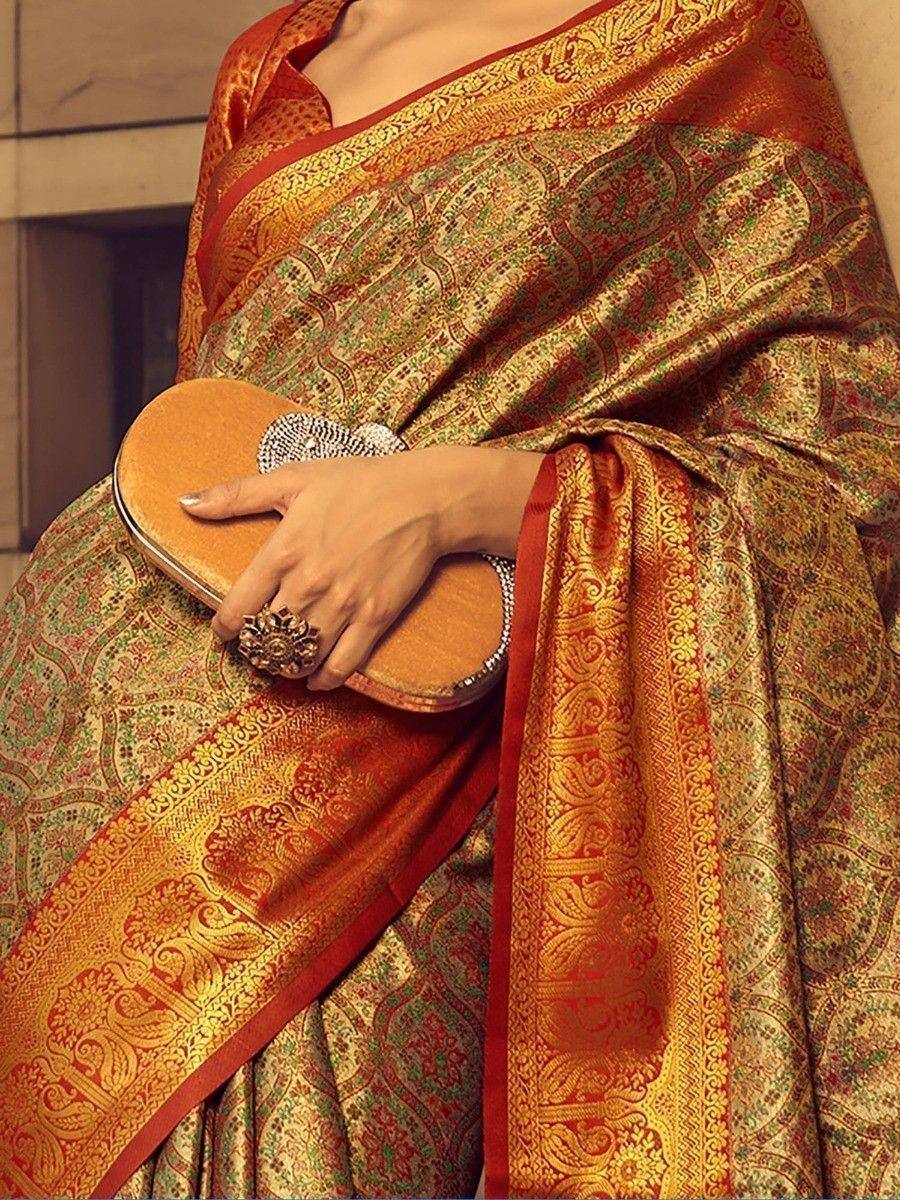Elegant Indian saree with intricate gold and red paisley patterns, paired with a matching clutch and statement ring.