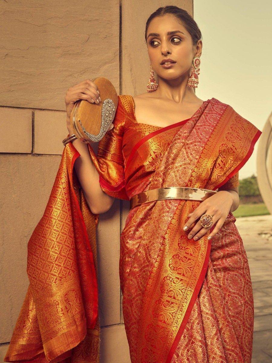 Elegant red and gold designer saree with intricate paisley patterns, paired with statement earrings and a metallic clutch.