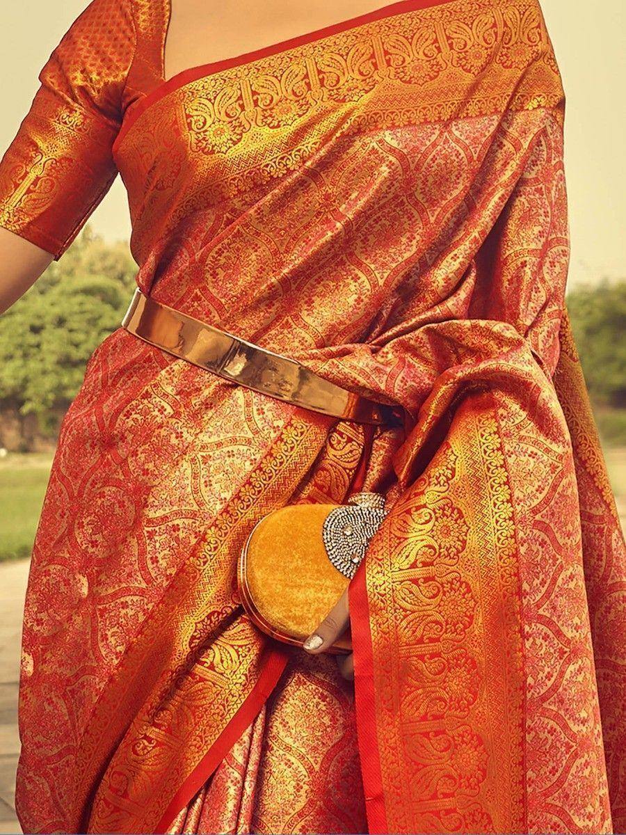 Red and gold designer saree with intricate paisley print, paired with a metallic belt and velvet clutch
