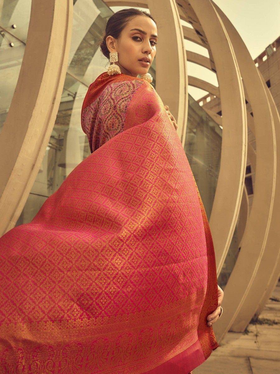 Woman in vibrant pink and gold designer saree with intricate patterns, styled with traditional earrings