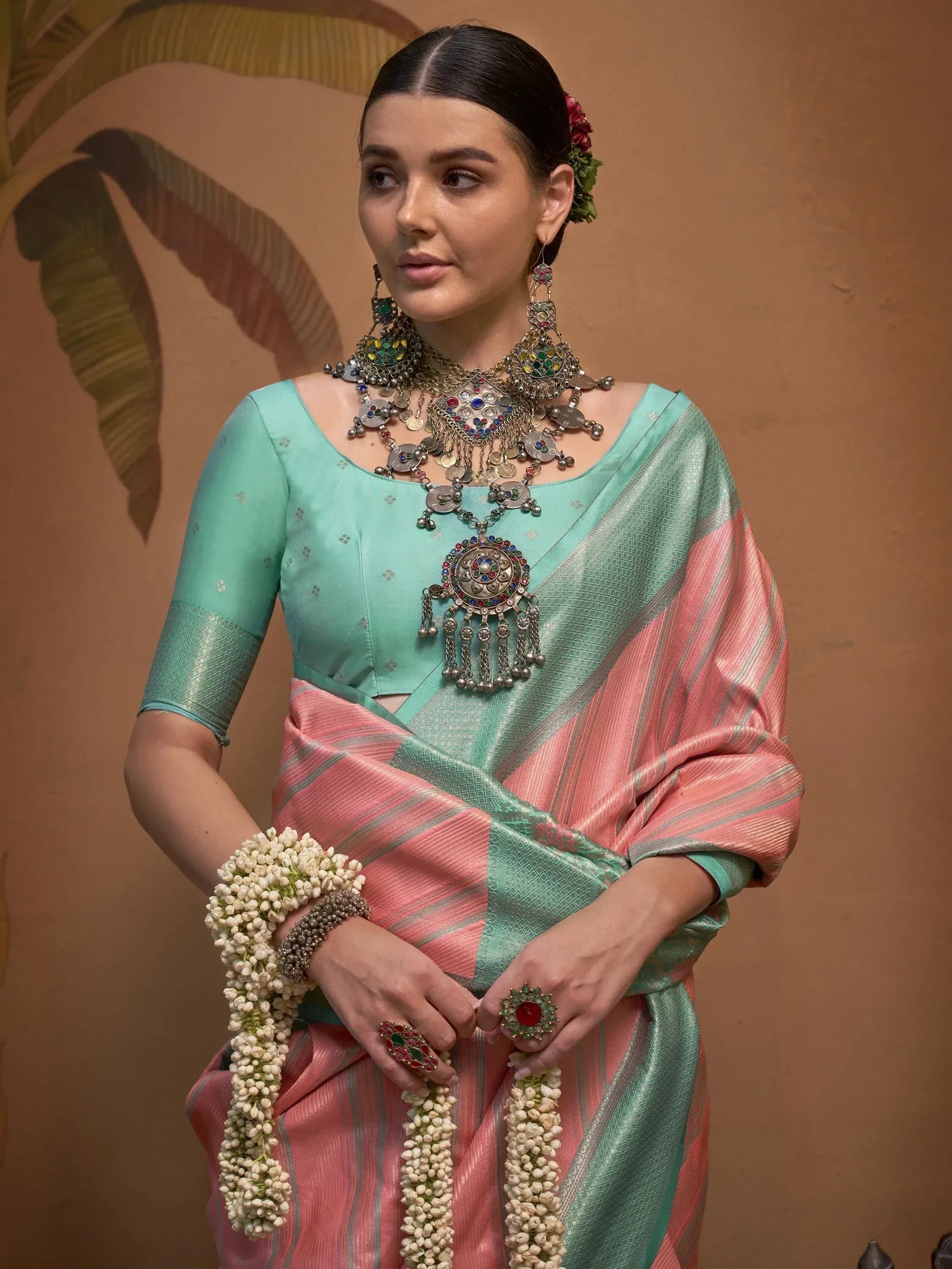 Woman in mint green and pink saree with traditional jewelry and floral accessories