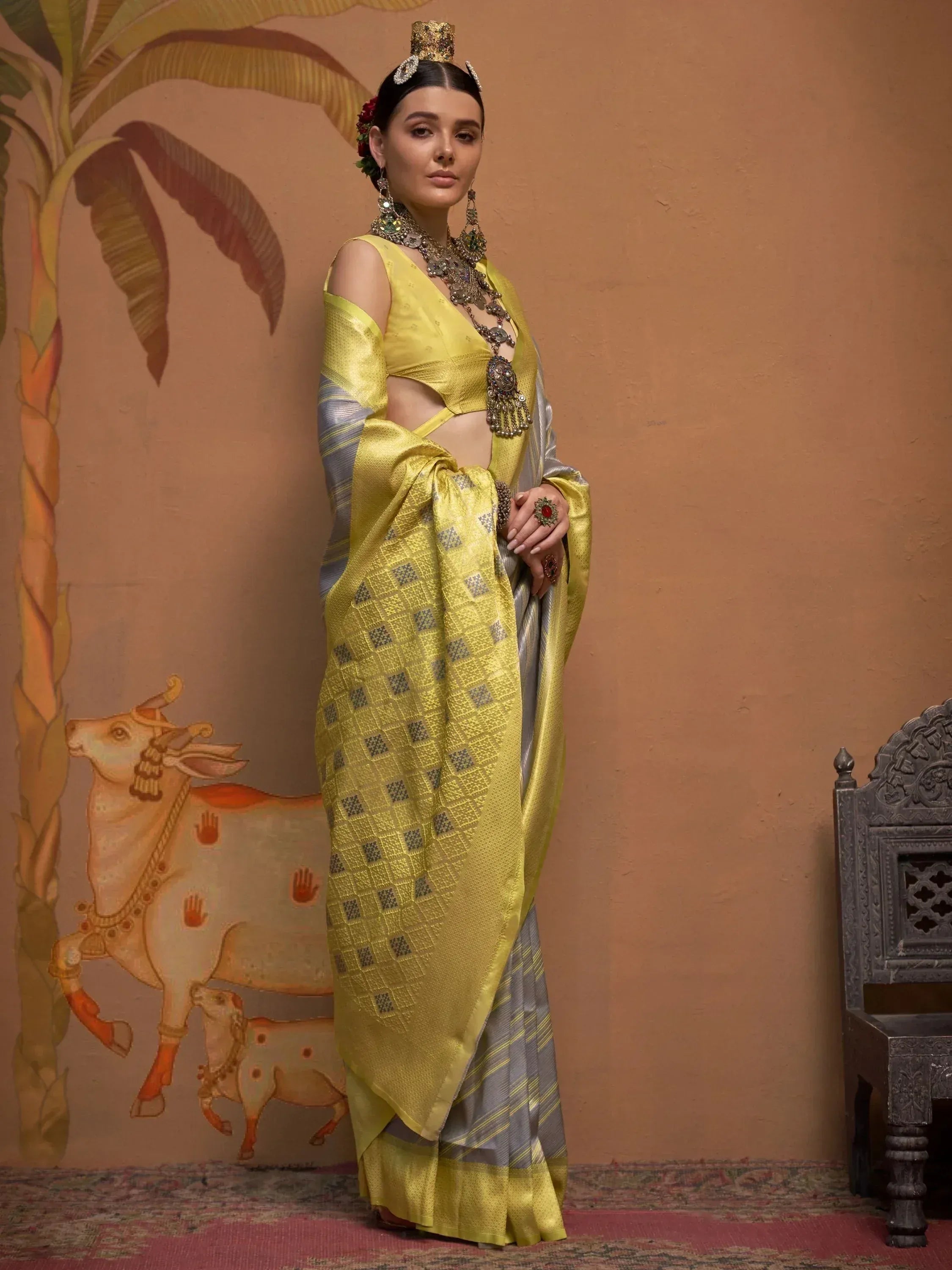 Yellow and silver designer saree with cut-out blouse, traditional jewelry, and ethnic backdrop
