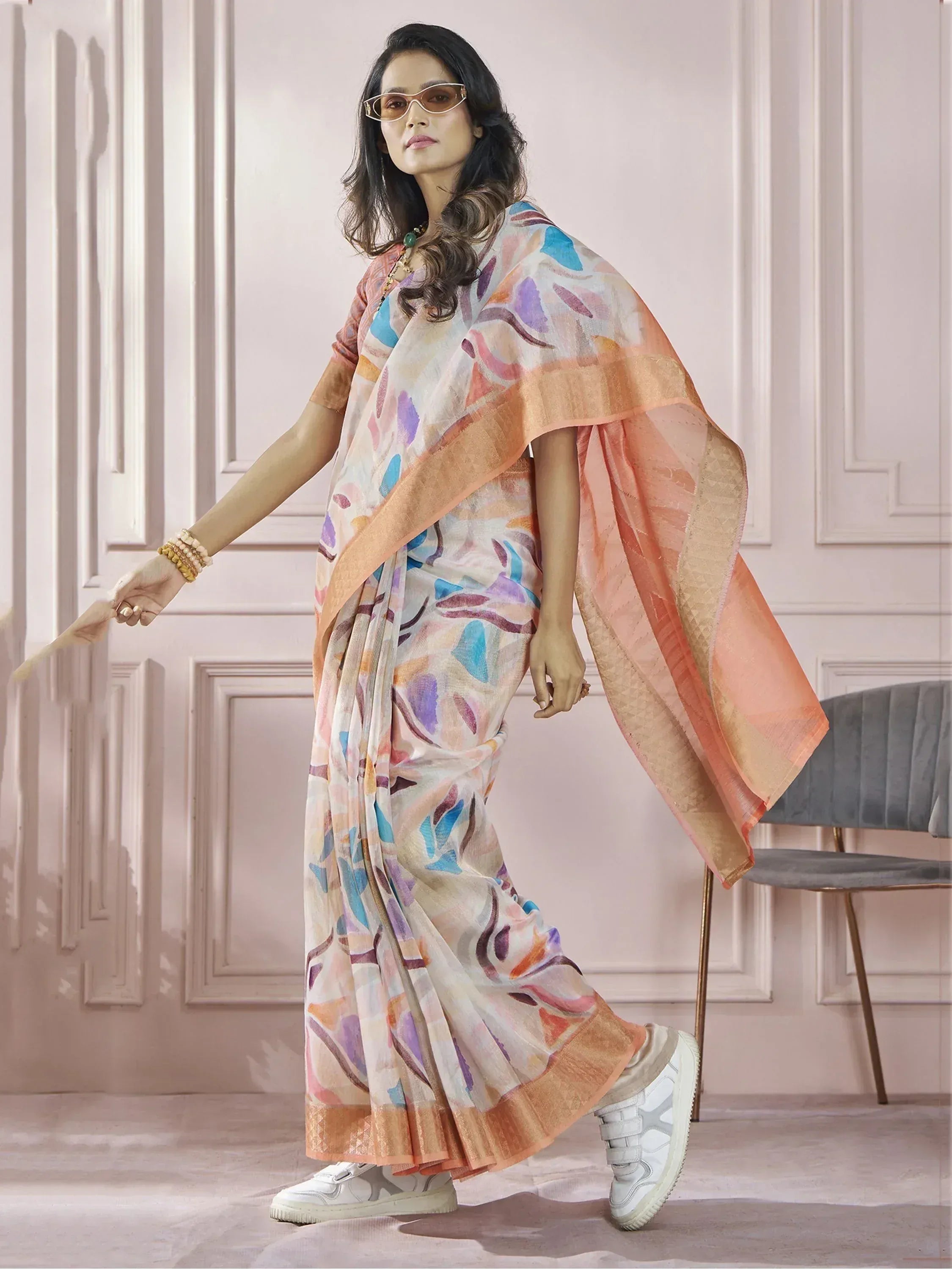 Woman in colorful printed saree with peach border, styled with sneakers and sunglasses for modern ethnic look