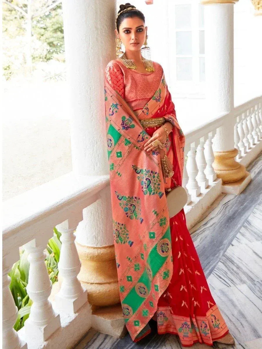Woman in vibrant pink and red ethnic saree with peacock print, gold jewelry, standing on balcony