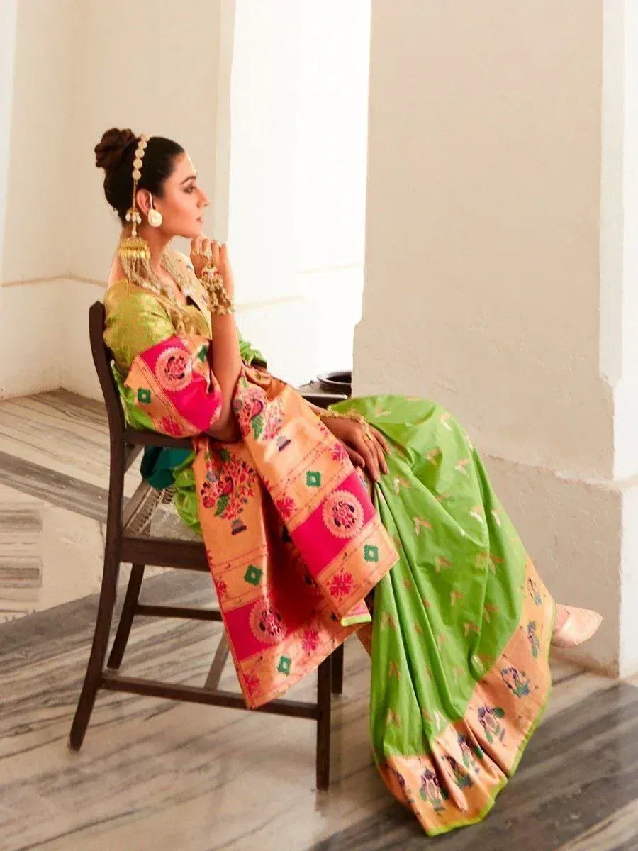 Woman in vibrant green and pink embroidered saree with traditional jewelry, seated elegantly