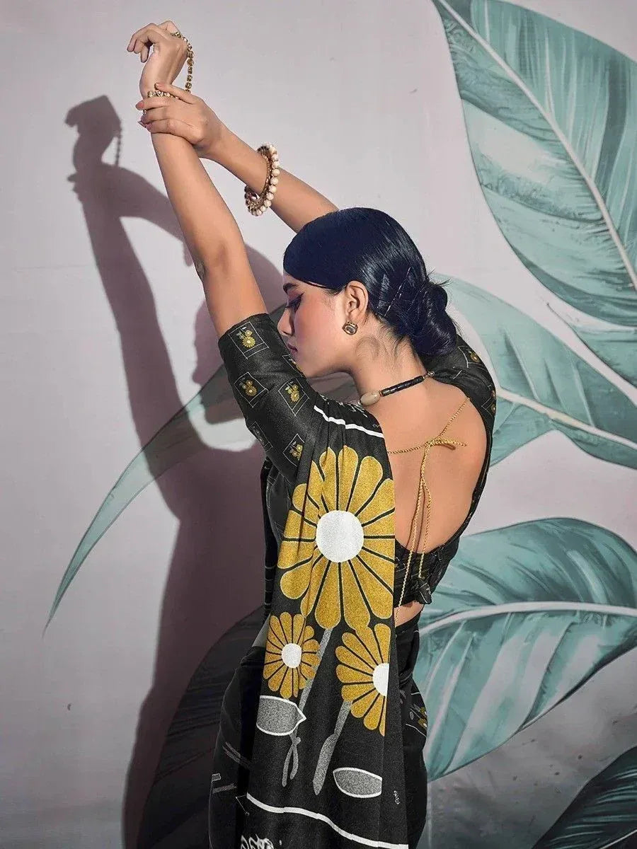 Woman in black saree with yellow floral print, backless blouse, and gold jewelry against leaf mural
