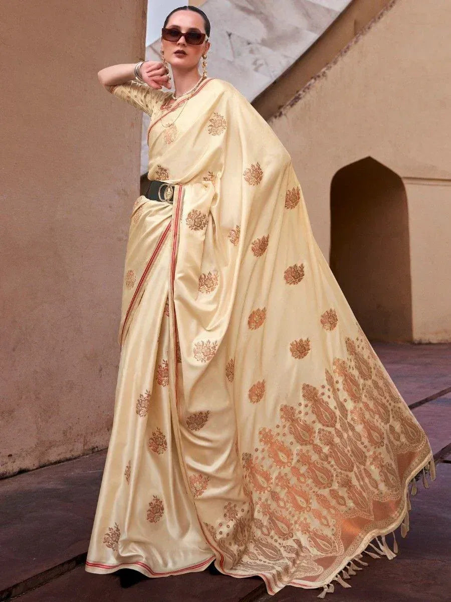 Cream silk saree with gold floral print, red border, and tassels, styled with belt for ethnic wear