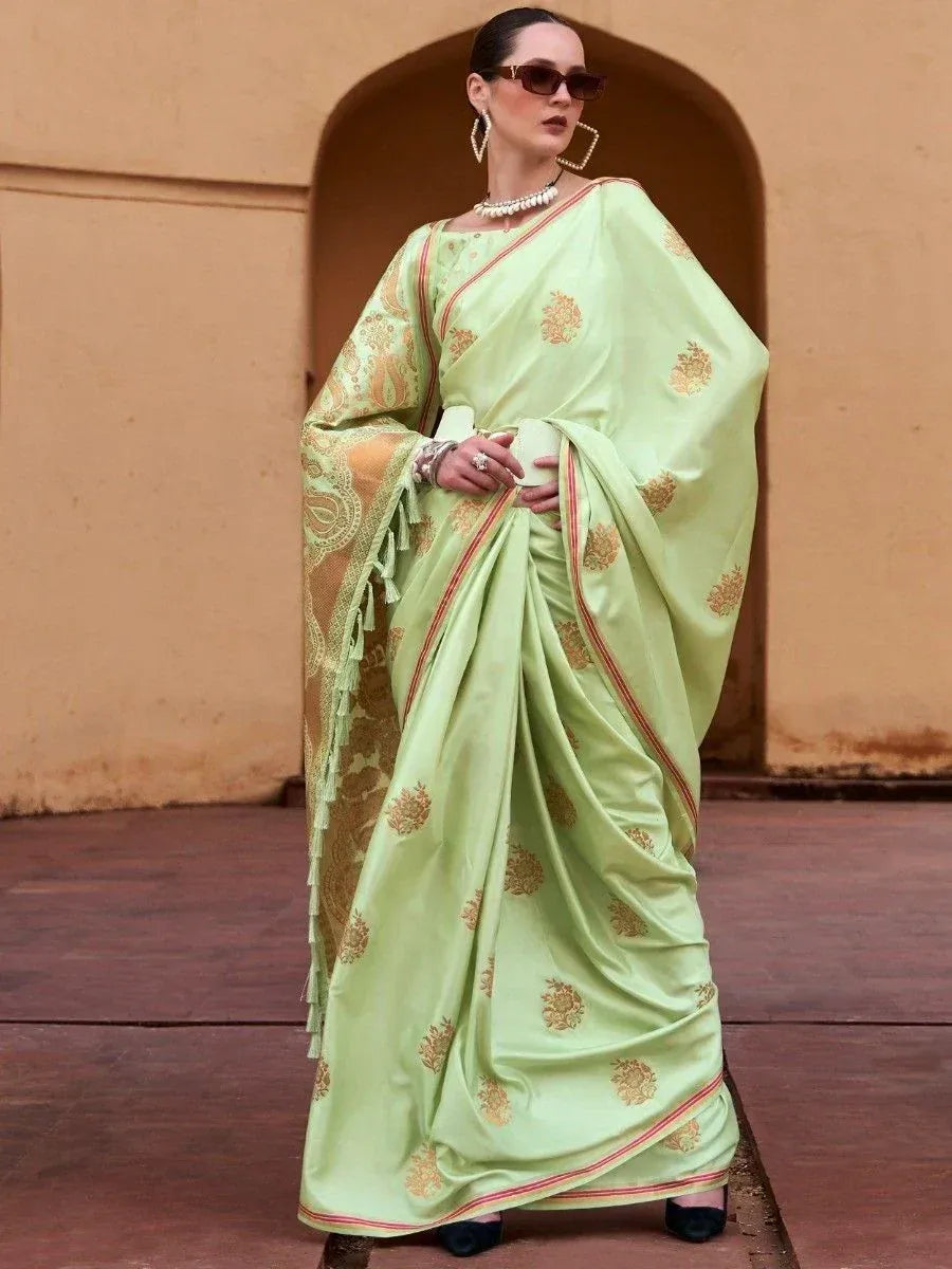 Light green designer saree with gold floral motifs and red border, styled with statement jewelry