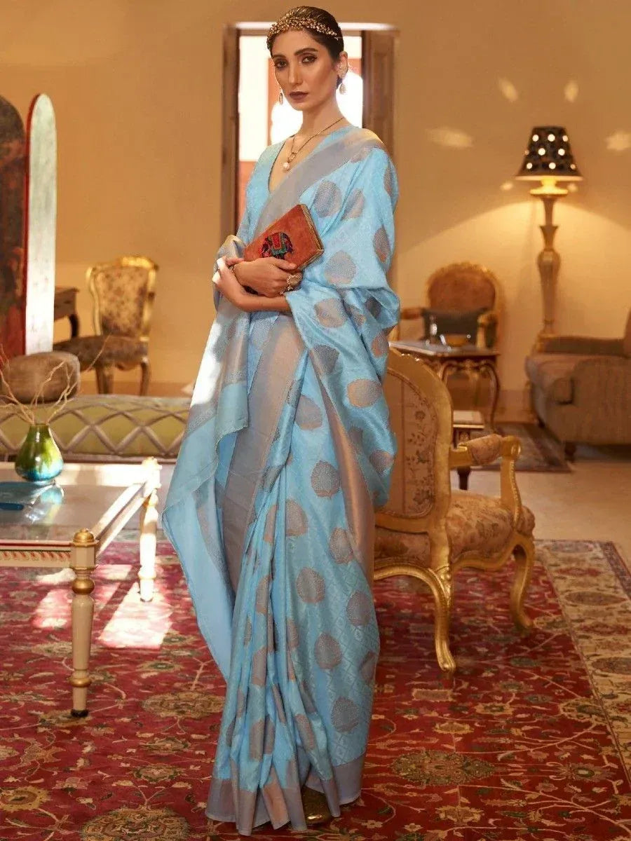 Elegant woman in light blue printed saree with gold motifs, holding clutch, styled for Indian ethnic occasions