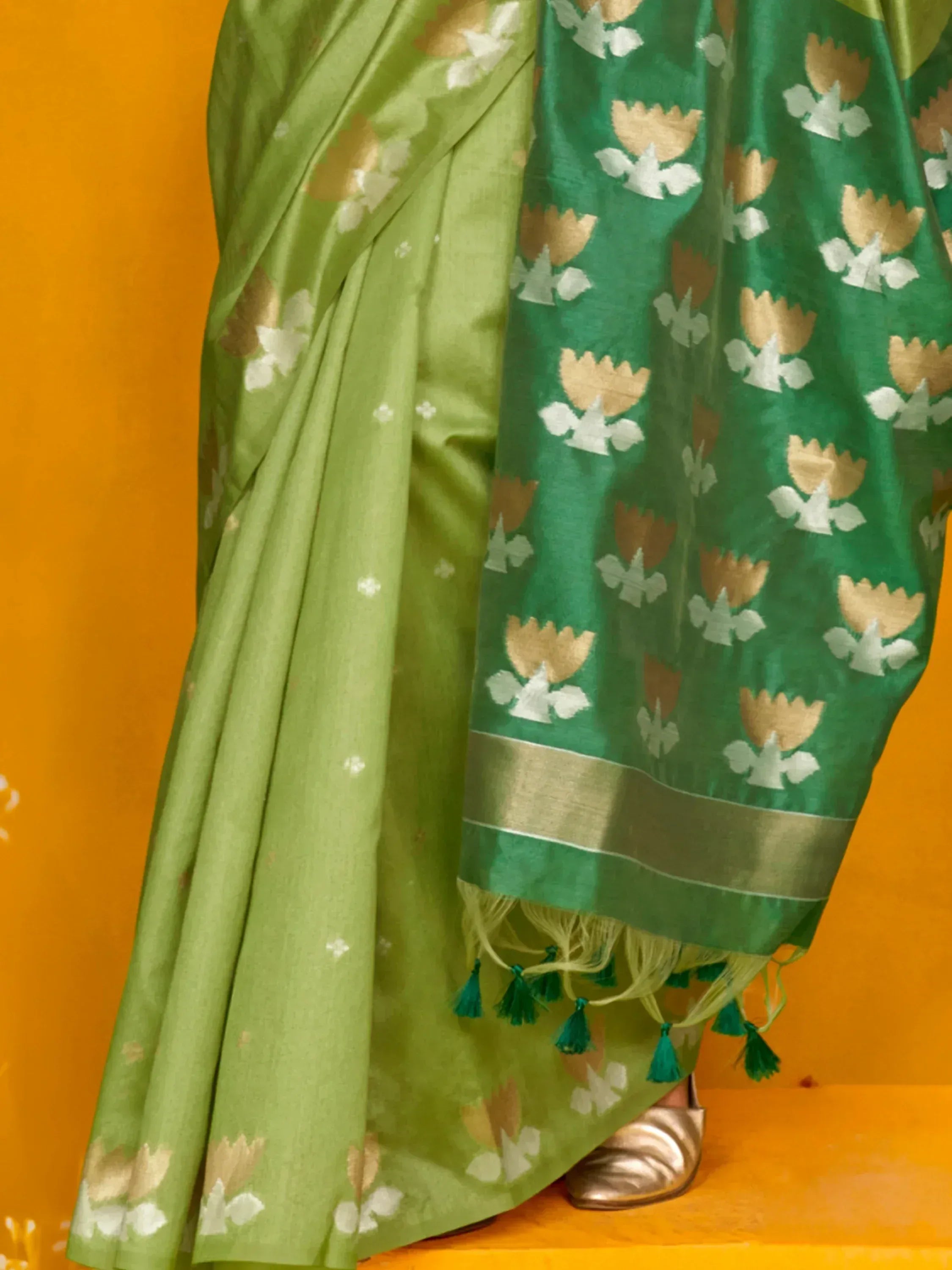 Green floral print saree with gold and white motifs, tassels, and border, styled with metallic sandals
