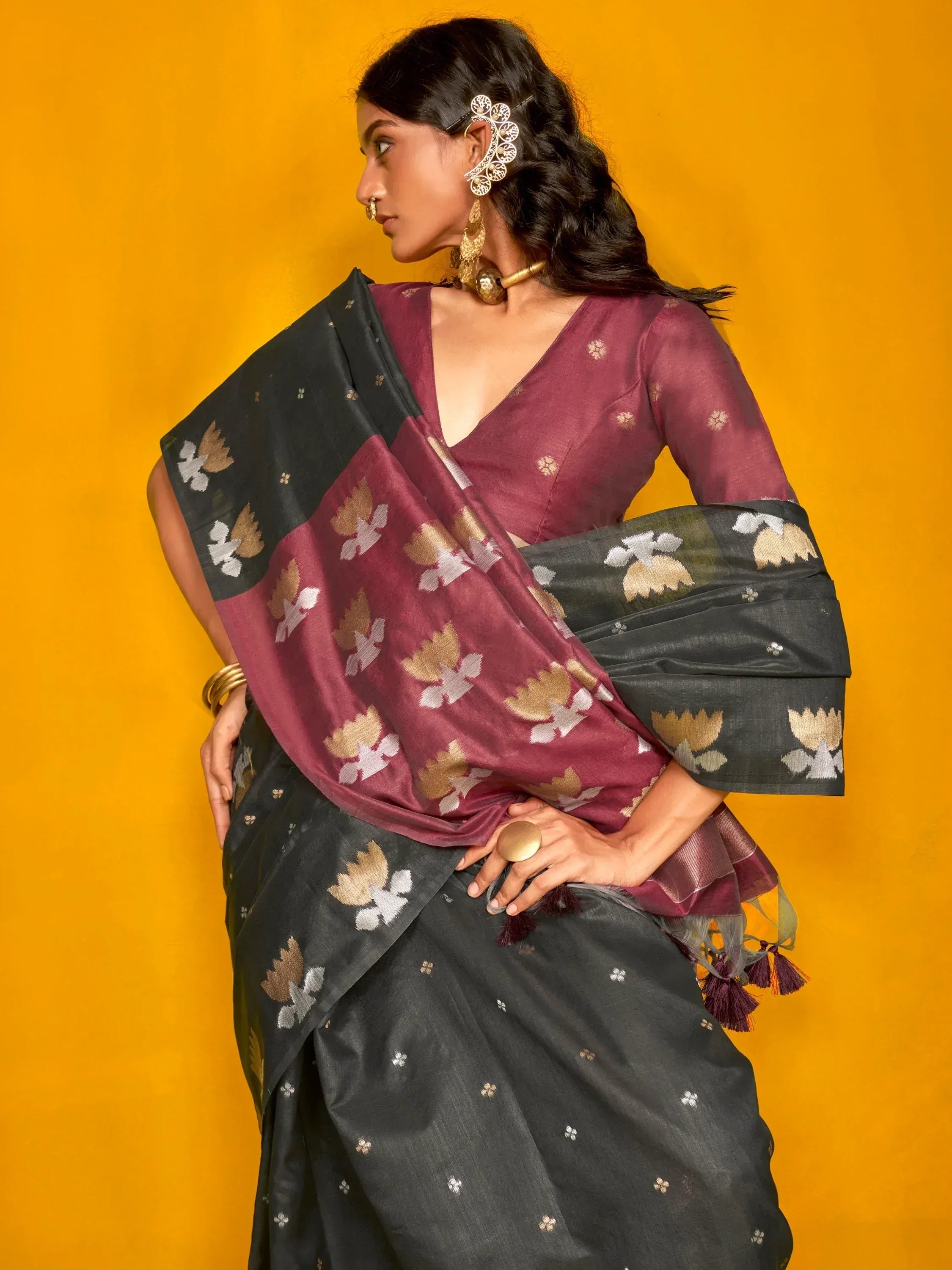Woman in elegant black and maroon floral saree with gold embroidery, styled with traditional jewelry against yellow backdrop