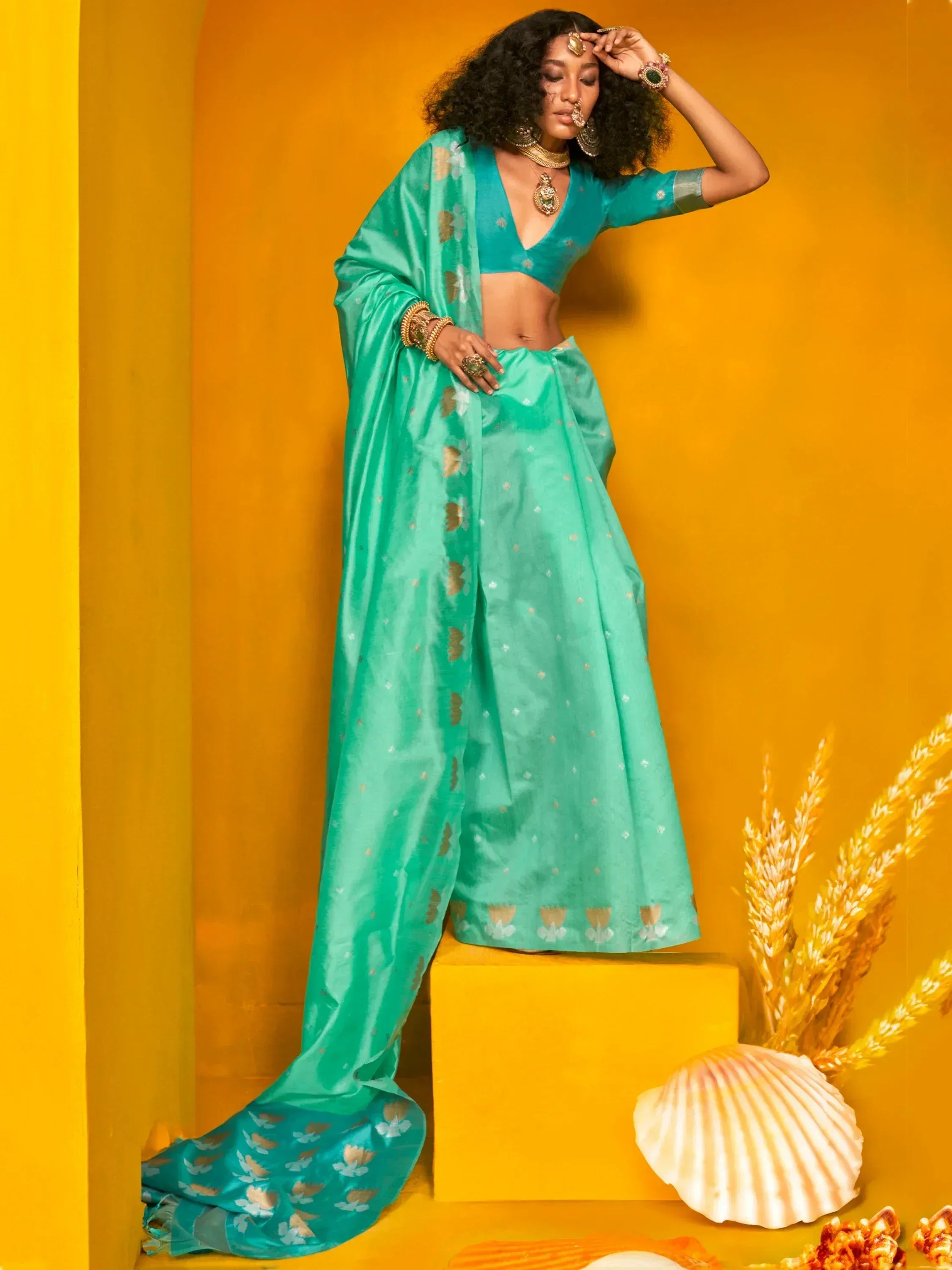 Teal designer lehenga choli with gold floral motifs, styled with traditional jewelry against a vibrant yellow backdrop