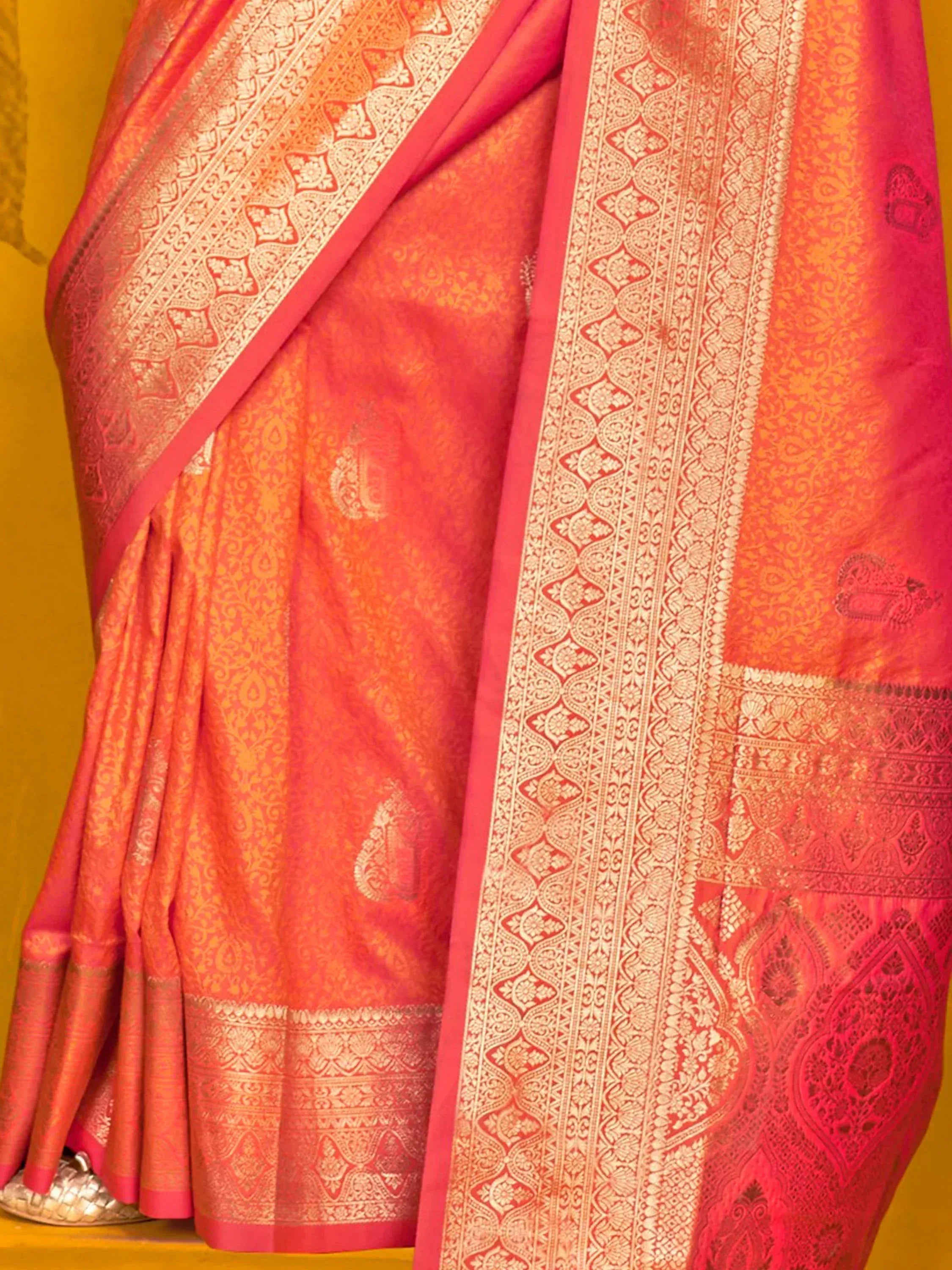 Vibrant coral pink saree with intricate gold zari work, perfect for Indian ethnic wear occasions.