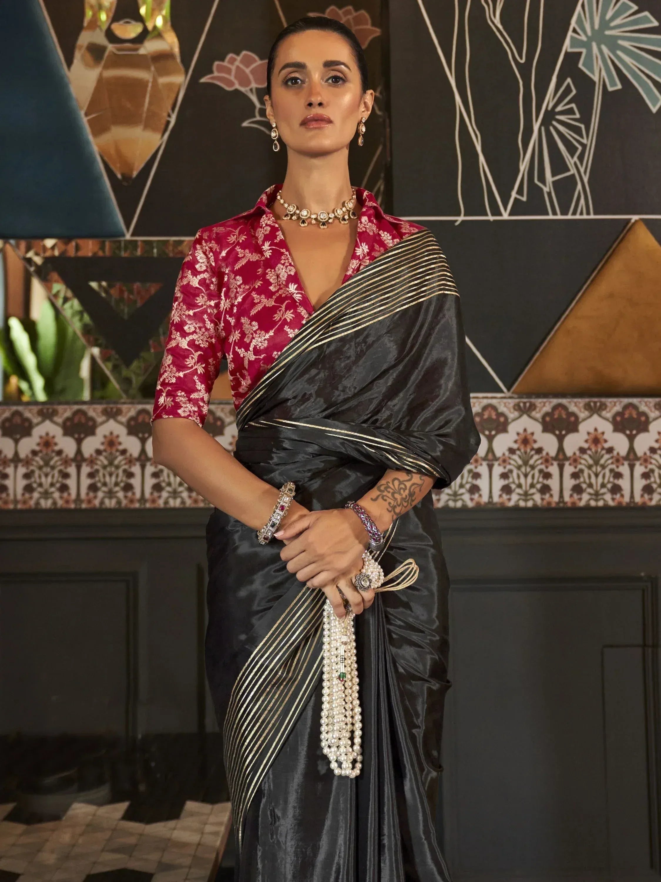Elegant black saree with gold stripes paired with a red floral blouse, perfect for Indian ethnic wear occasions.