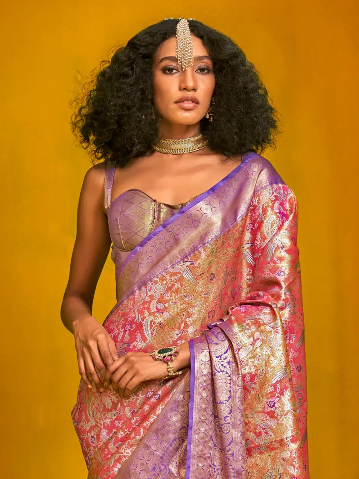 Elegant woman in vibrant pink and purple designer saree with intricate gold embroidery and traditional jewelry