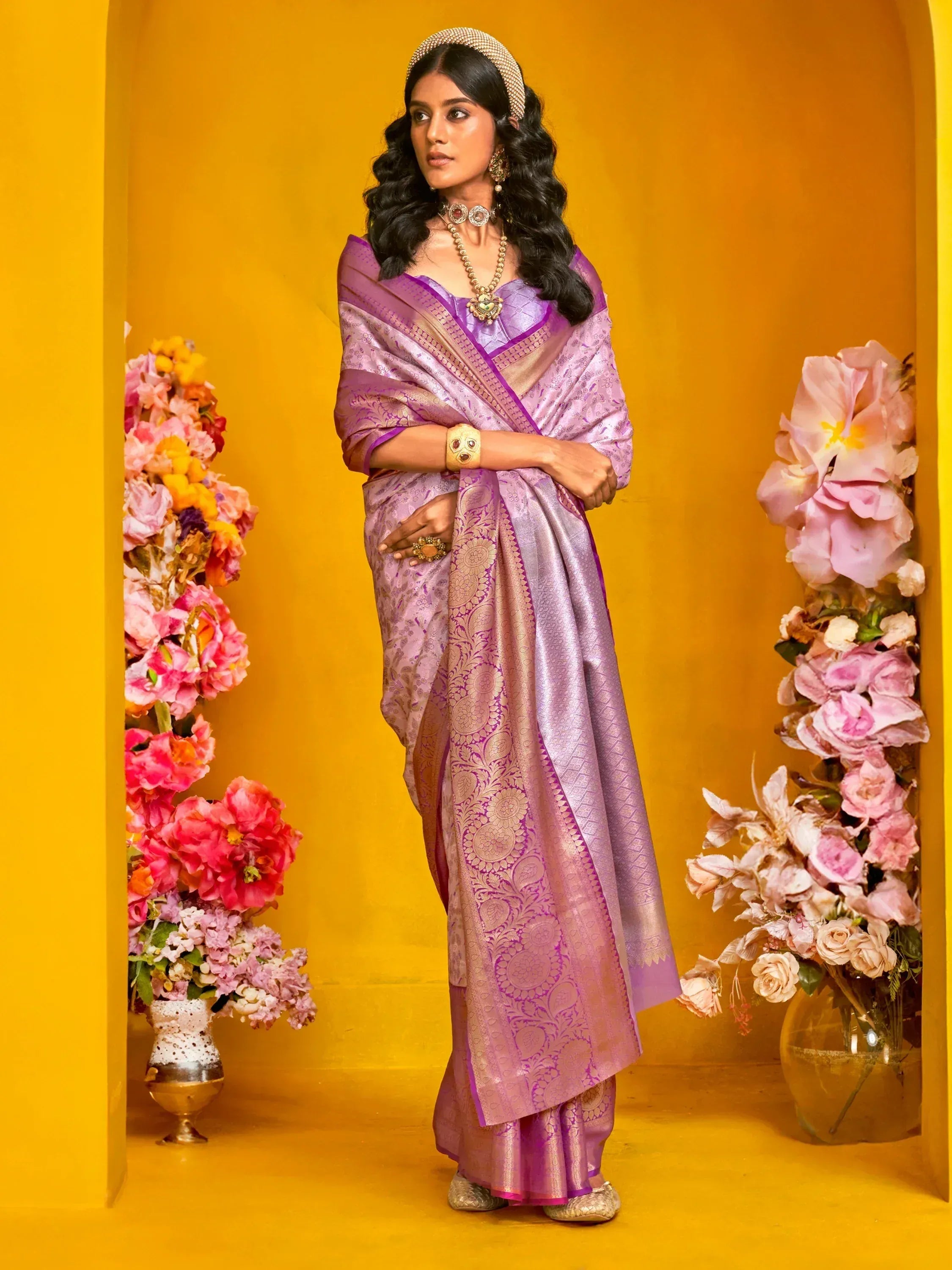 Purple designer saree with gold embroidery, styled with traditional jewelry against a vibrant yellow backdrop.