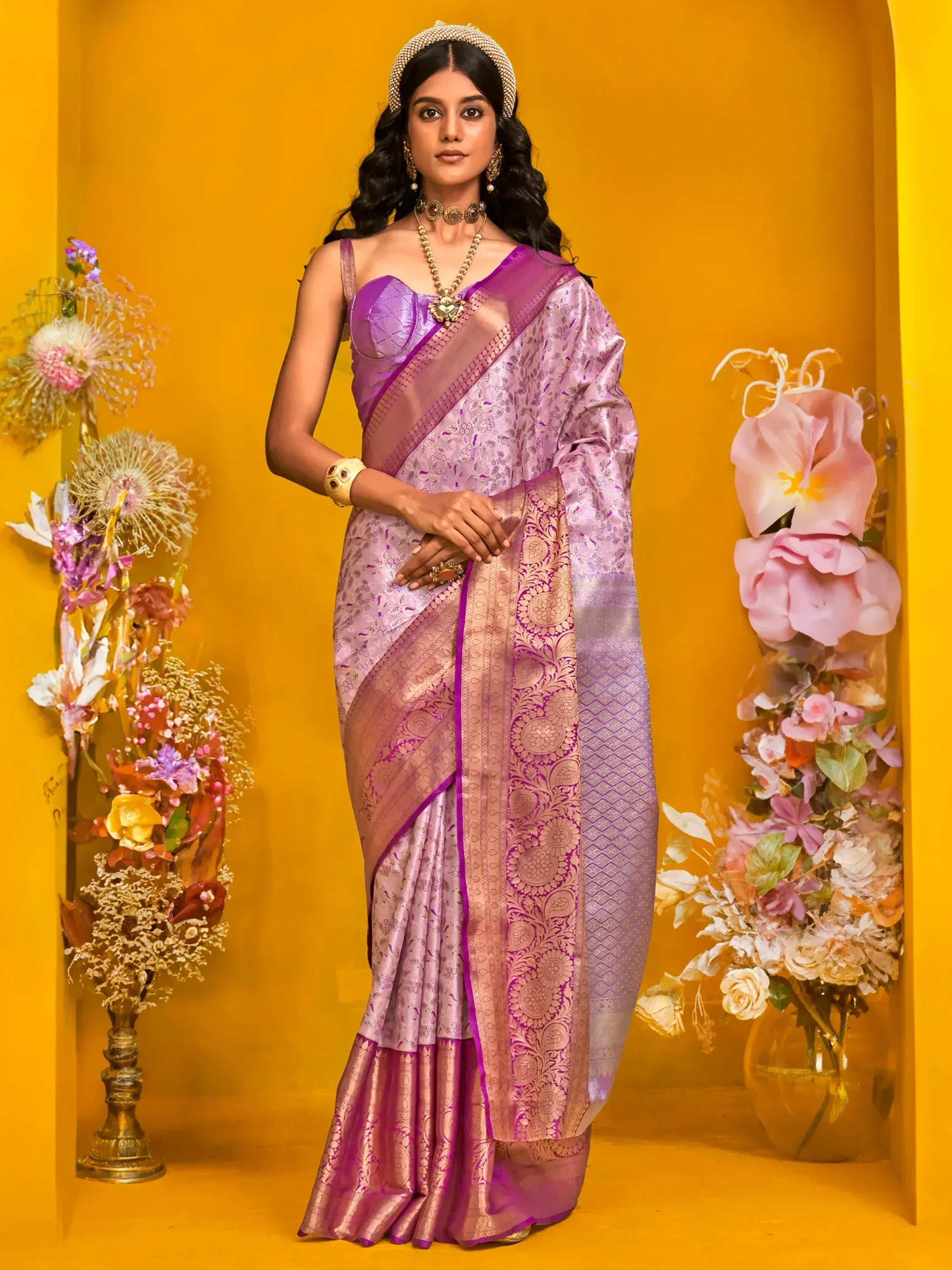 Elegant purple designer saree with intricate gold patterns, paired with traditional jewelry and floral decor.