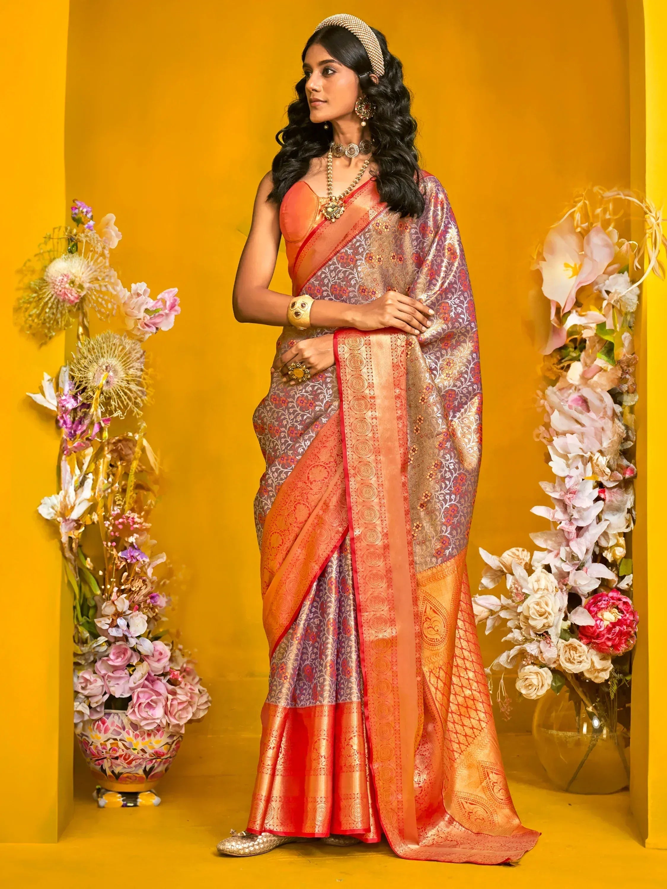 Elegant woman in designer saree with intricate patterns and vibrant orange border, styled with traditional jewelry.