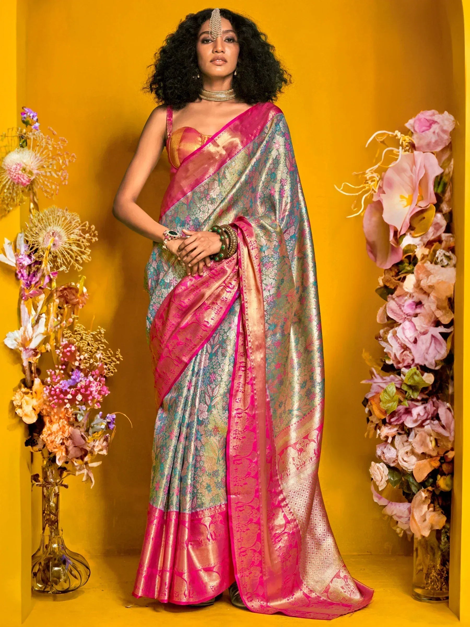 Elegant pink and gold floral saree with intricate designs, styled with traditional jewelry against a vibrant yellow backdrop.
