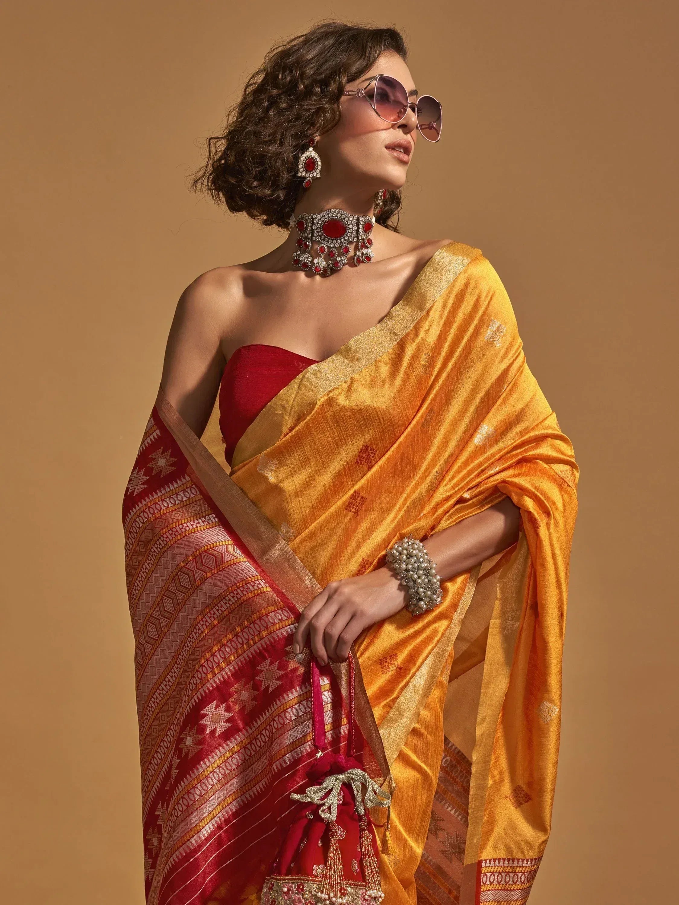 Woman in vibrant yellow and red ethnic saree with traditional jewelry and sunglasses
