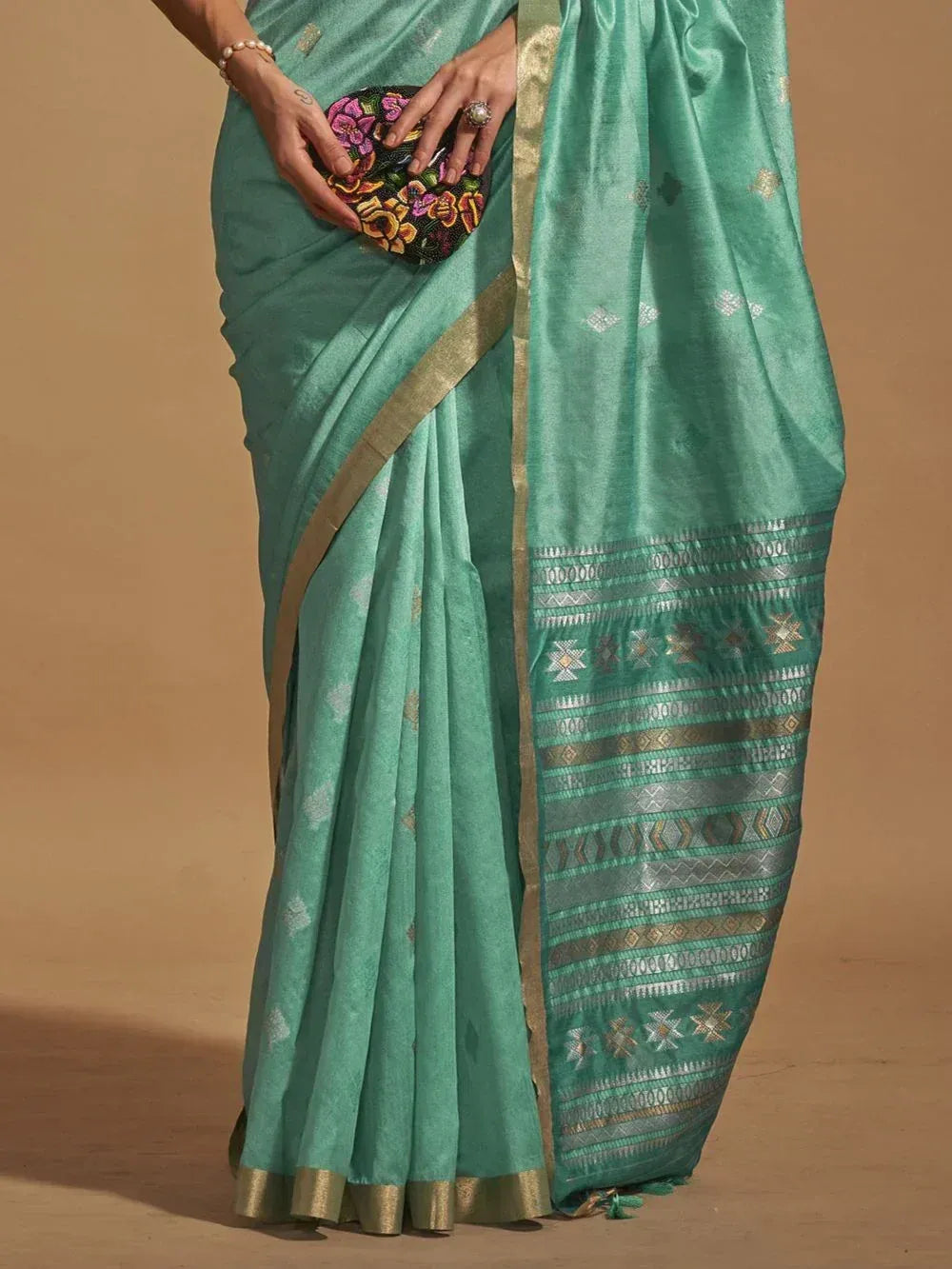 Teal silk saree with gold border and geometric pallu, paired with floral clutch for ethnic wear