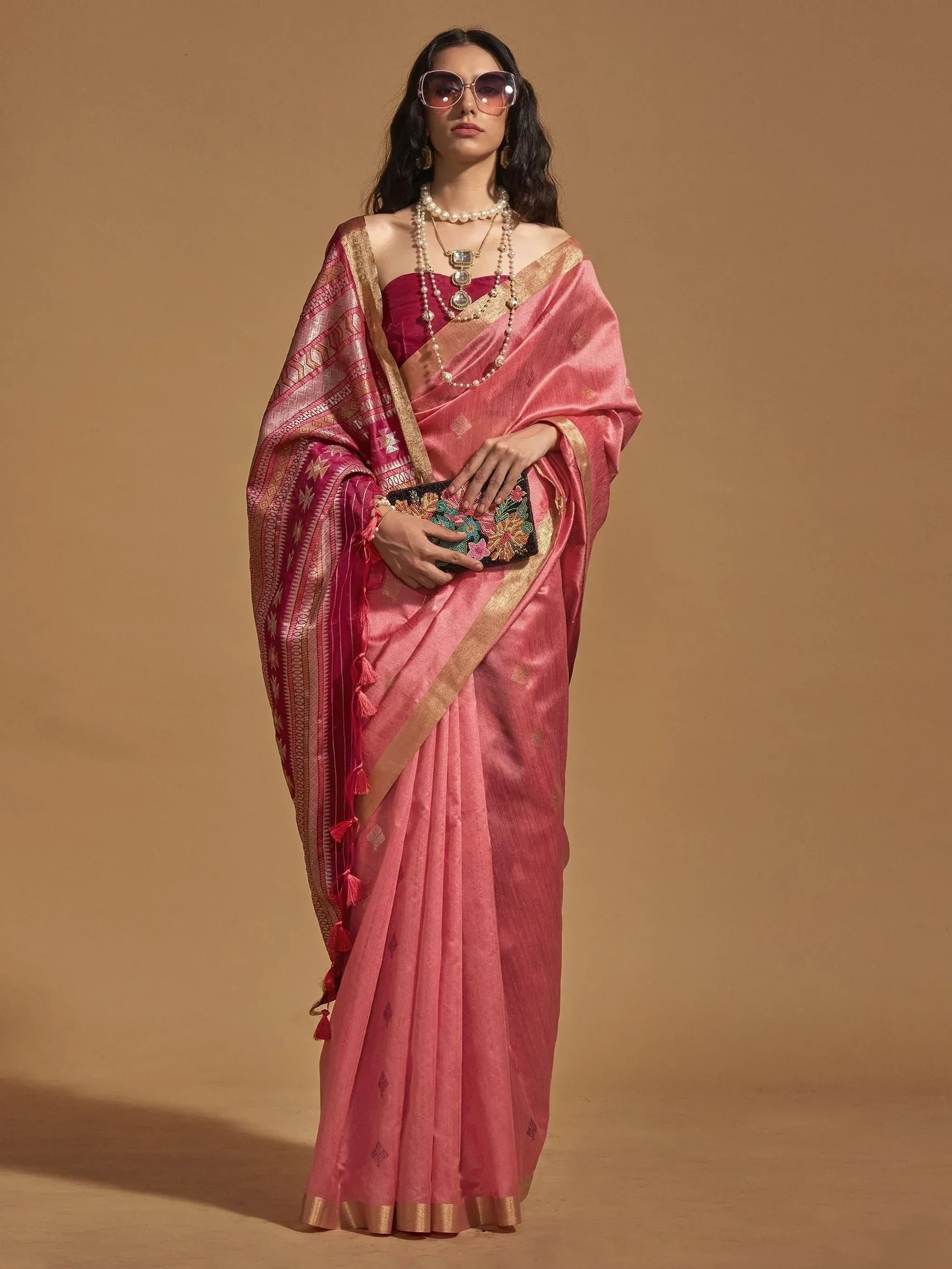 Pink ethnic saree with gold border and tassels, paired with pearl jewelry and floral clutch