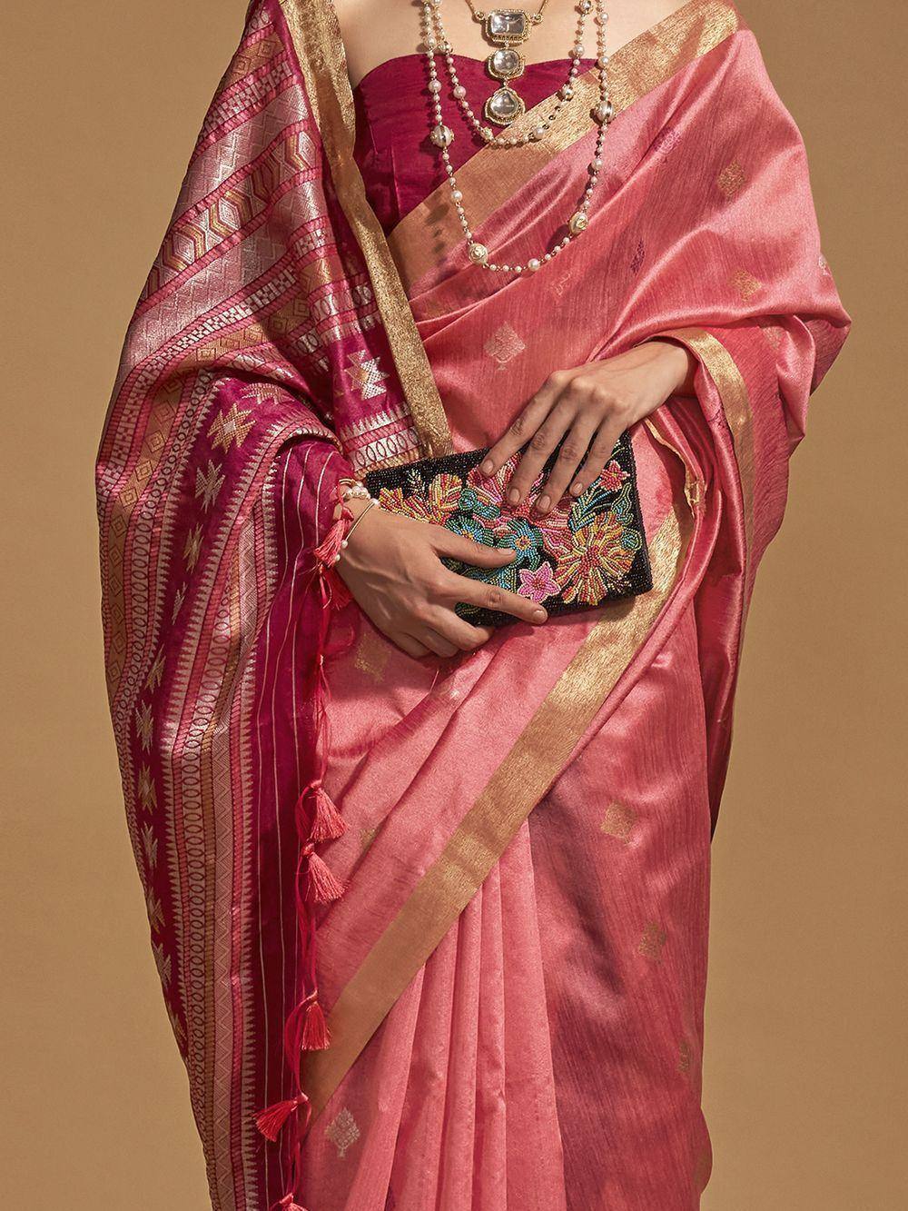 Pink silk saree with gold border and geometric pallu, paired with embroidered clutch and pearl jewelry