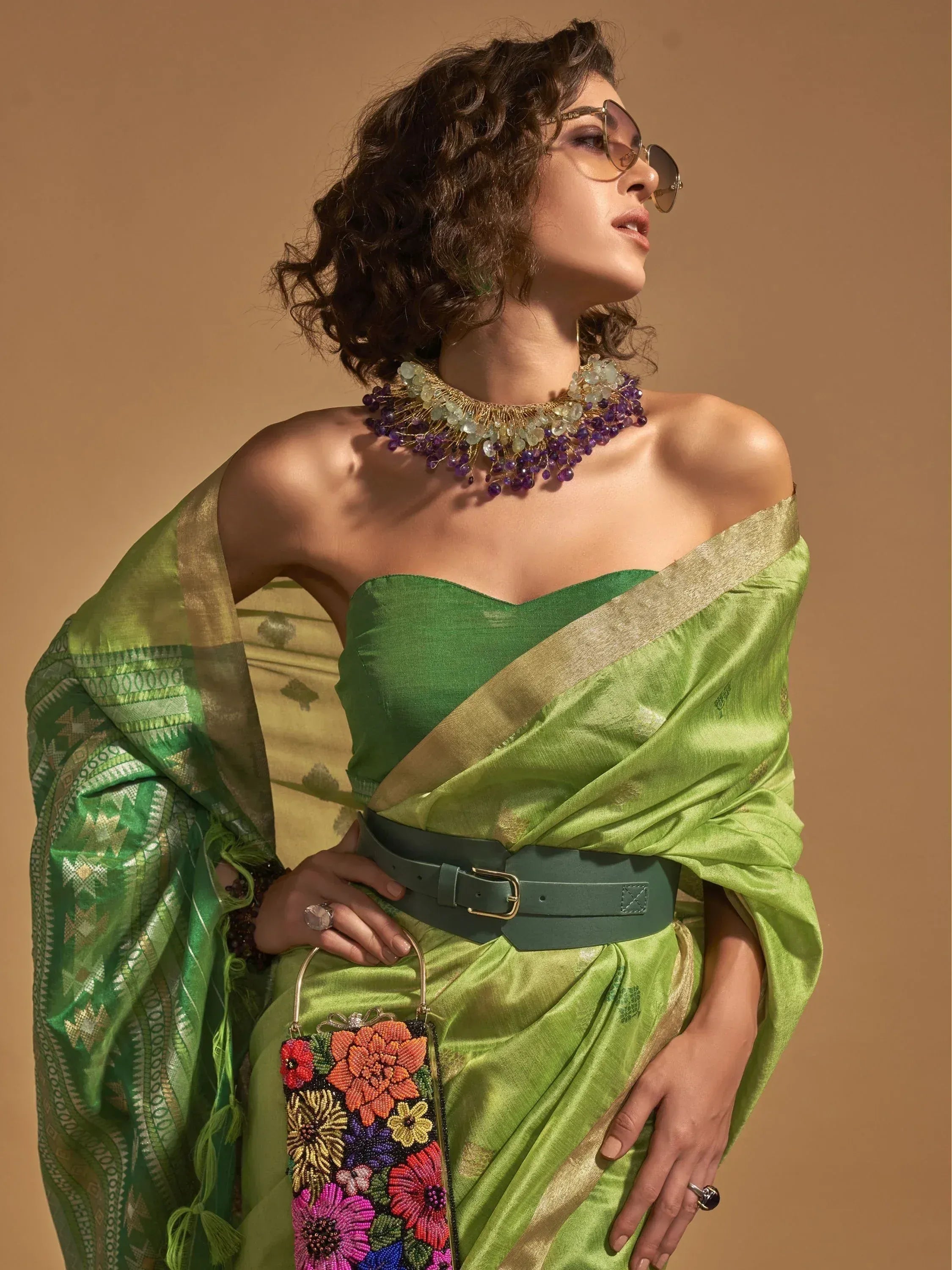 Green saree with gold border, off-shoulder blouse, statement necklace, and floral beaded clutch for ethnic wear