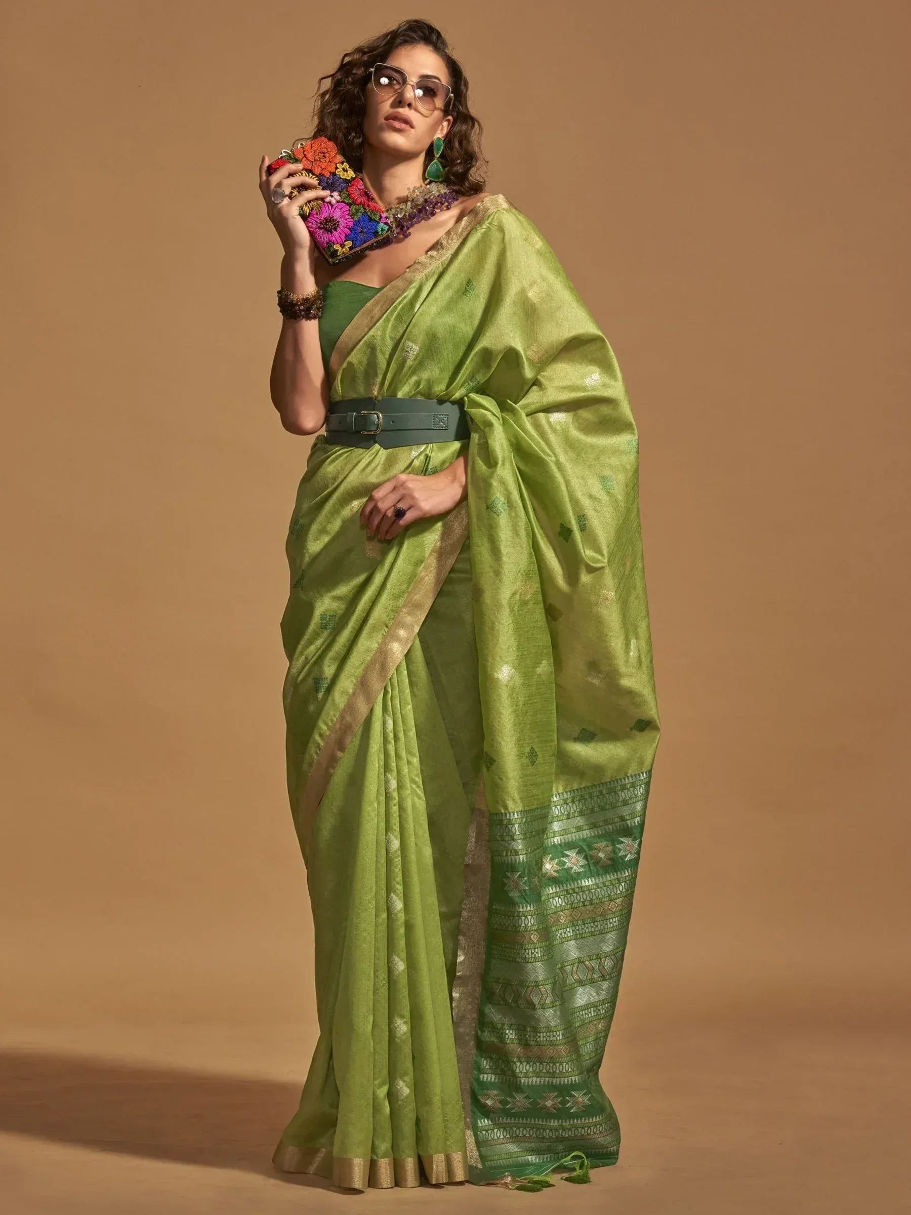 Woman in vibrant green ethnic saree with gold border, floral clutch, and statement jewelry