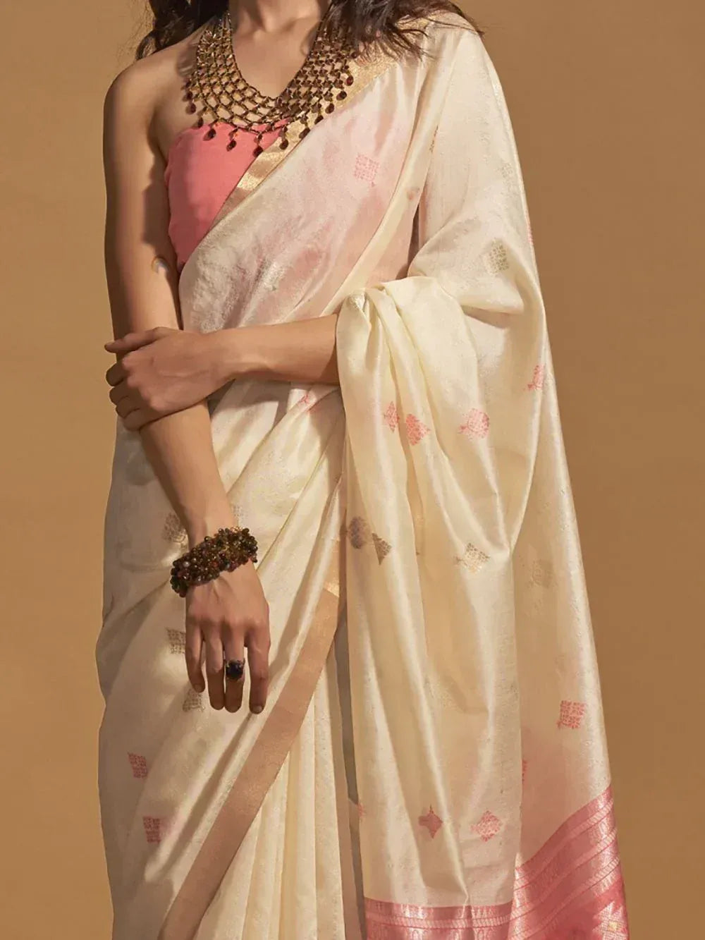 Cream saree with pink motifs and border, paired with pink blouse and gold jewelry for ethnic wear