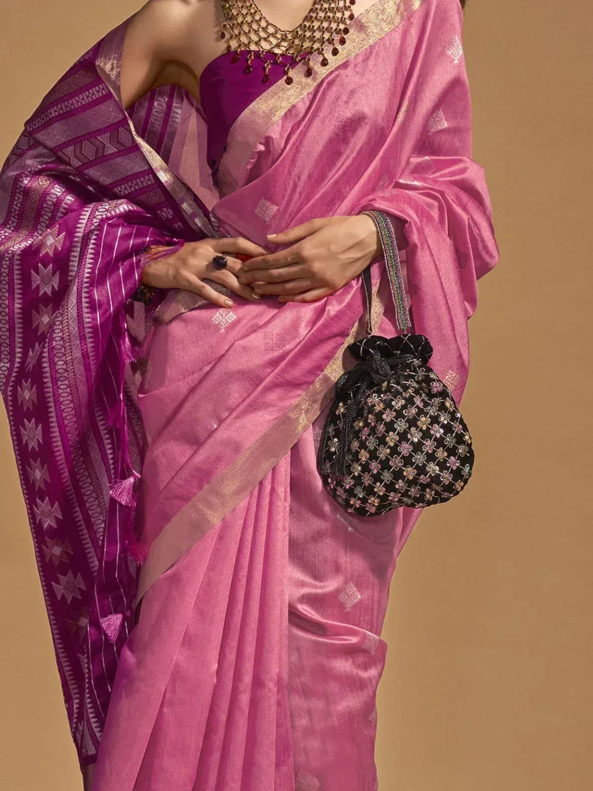 Pink silk saree with purple geometric border, gold trim, and embellished black potli bag for ethnic wear
