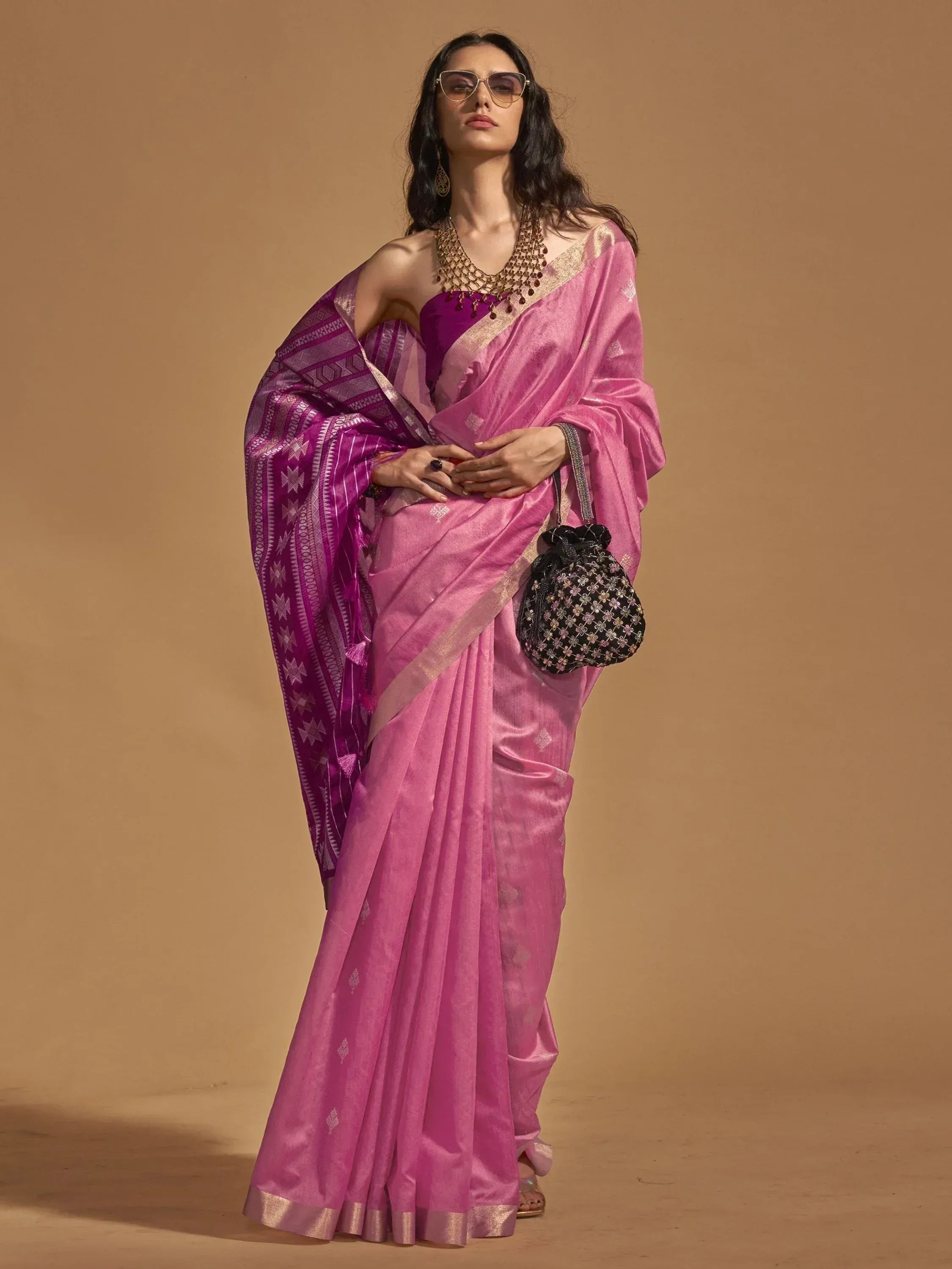 Pink designer saree with purple border, ethnic wear for women, paired with statement jewelry and potli bag