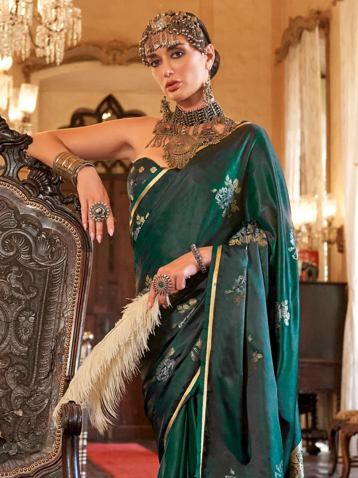 Elegant woman in green designer saree with gold embroidery, traditional Indian jewelry, and feather fan.