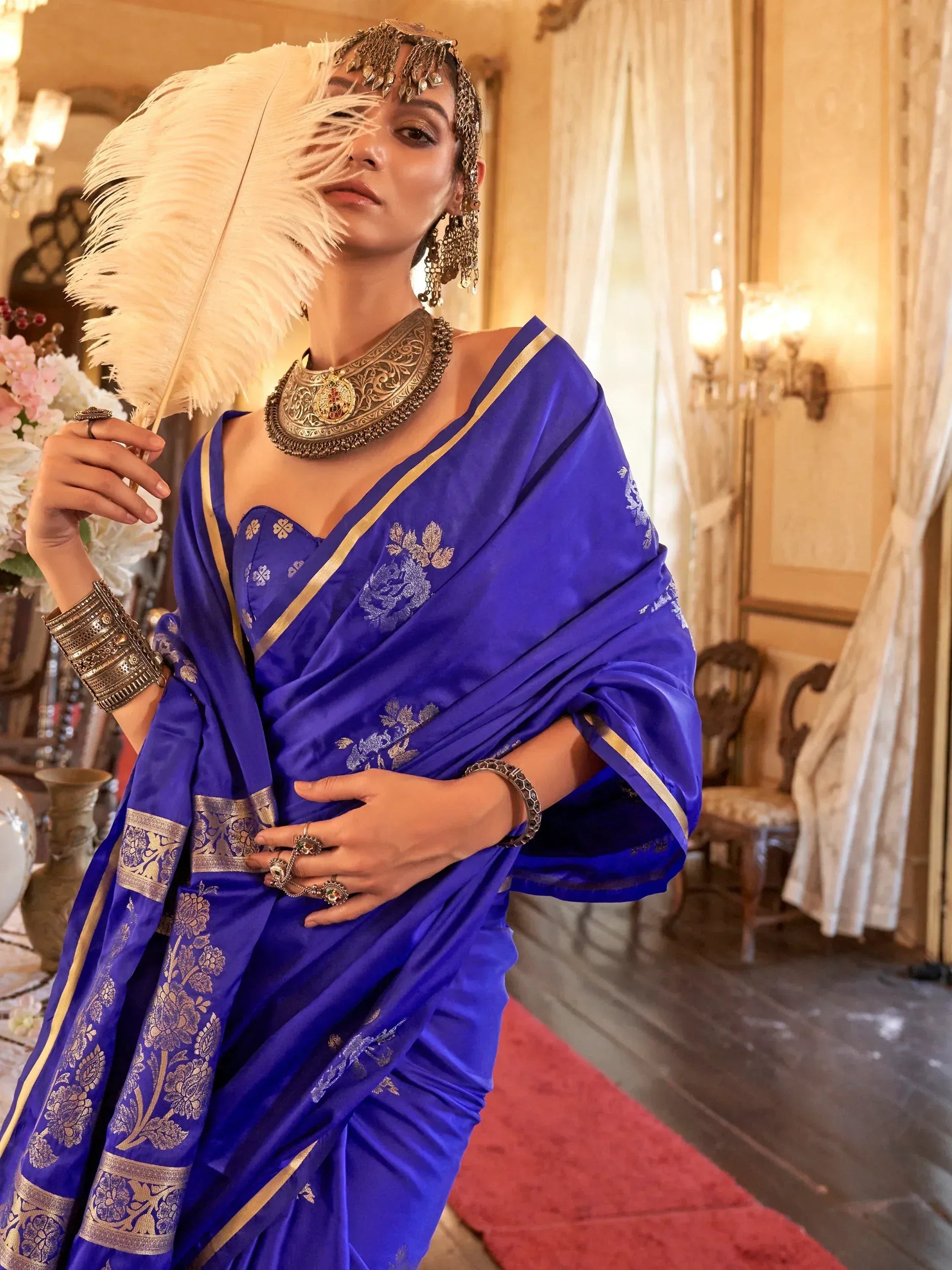 Royal blue saree with gold floral embroidery, traditional Indian ethnic wear, paired with ornate jewelry and feather fan