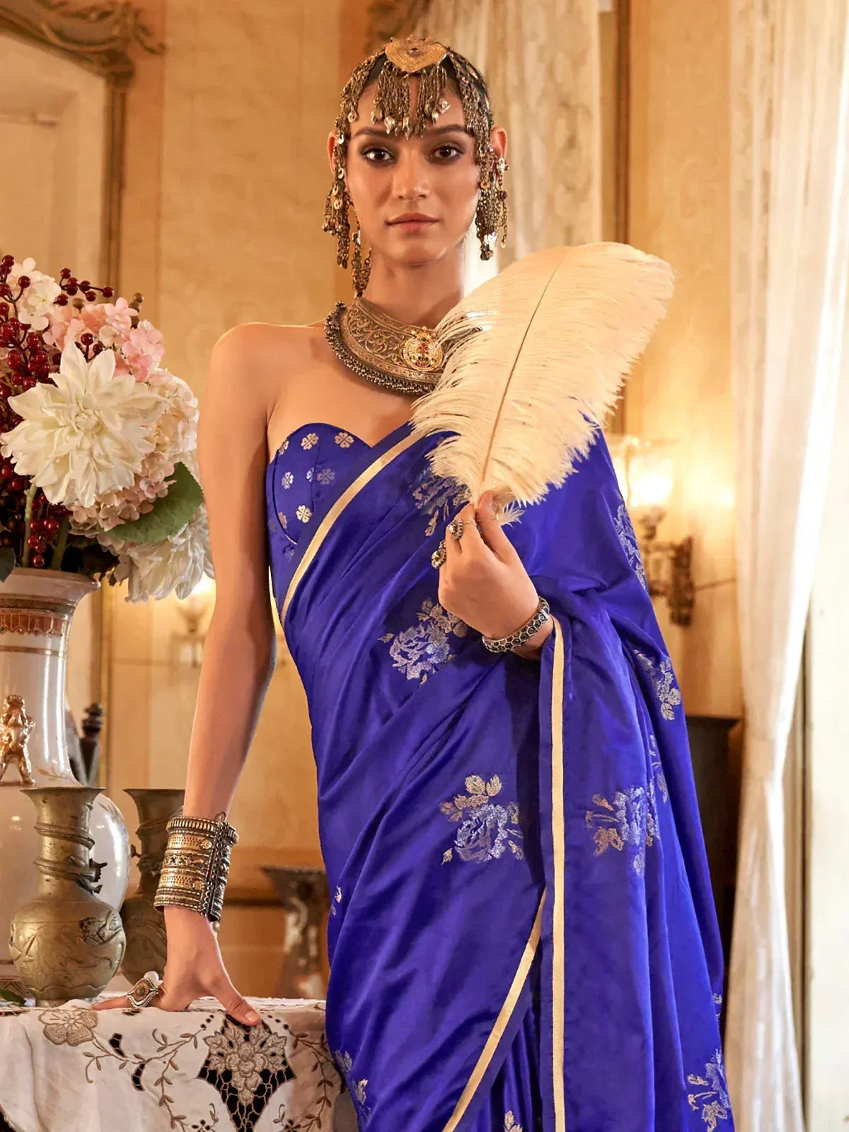 Royal blue embroidered saree with gold detailing, traditional Indian jewelry, and feather accessory for ethnic wear