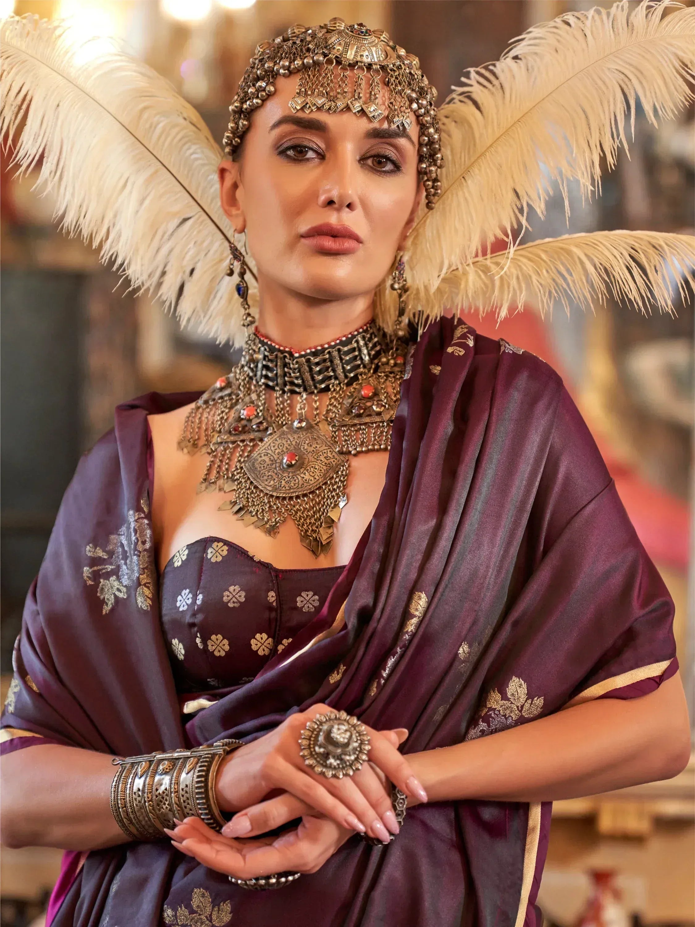 Elegant woman in purple ethnic gown with gold embroidery, feathered headpiece, and antique jewelry