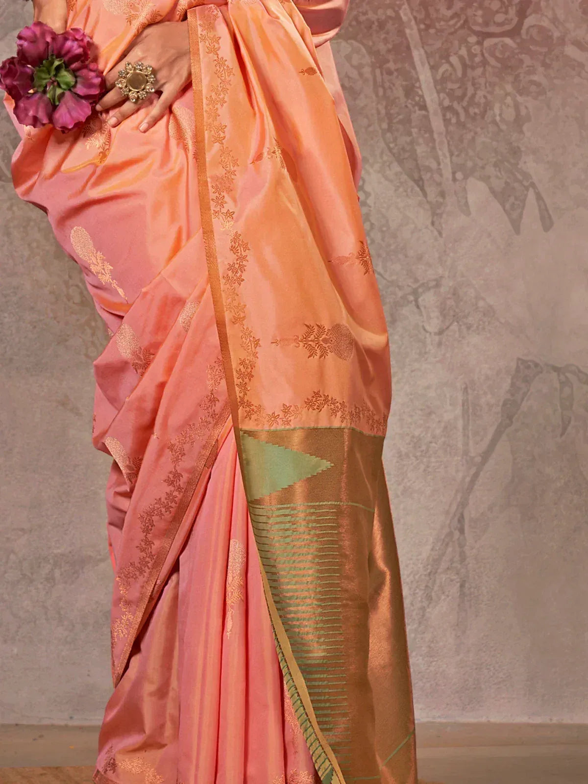 Peach silk saree with gold floral embroidery and green border, styled with flowers and statement ring