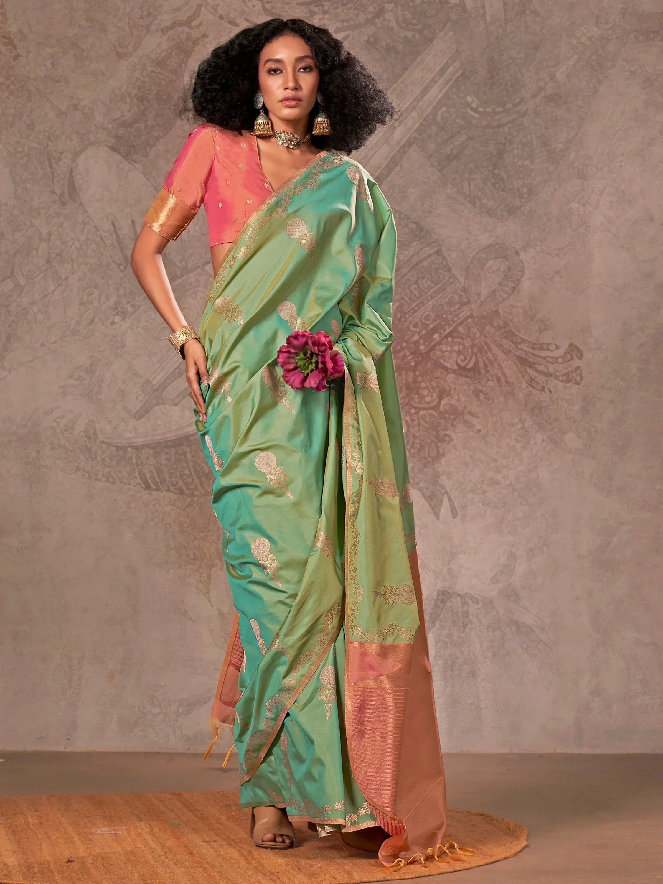 Green and pink designer saree with gold motifs, paired with matching blouse and traditional jewelry