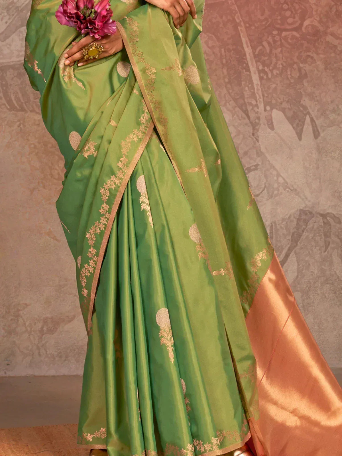 Green silk saree with gold floral embroidery and contrasting peach border, styled with pink flowers