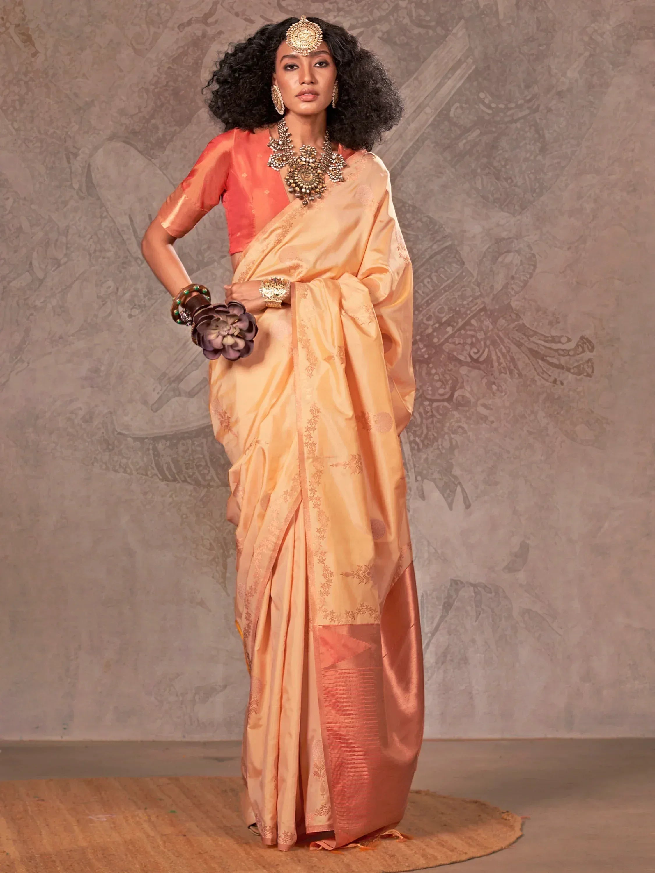 Woman in peach silk saree with gold embroidery, matching blouse, and traditional Indian jewelry