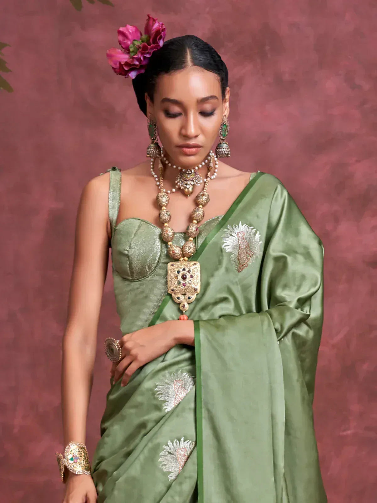 Elegant green saree with floral embroidery, paired with traditional jewelry and pink floral hair accessory.