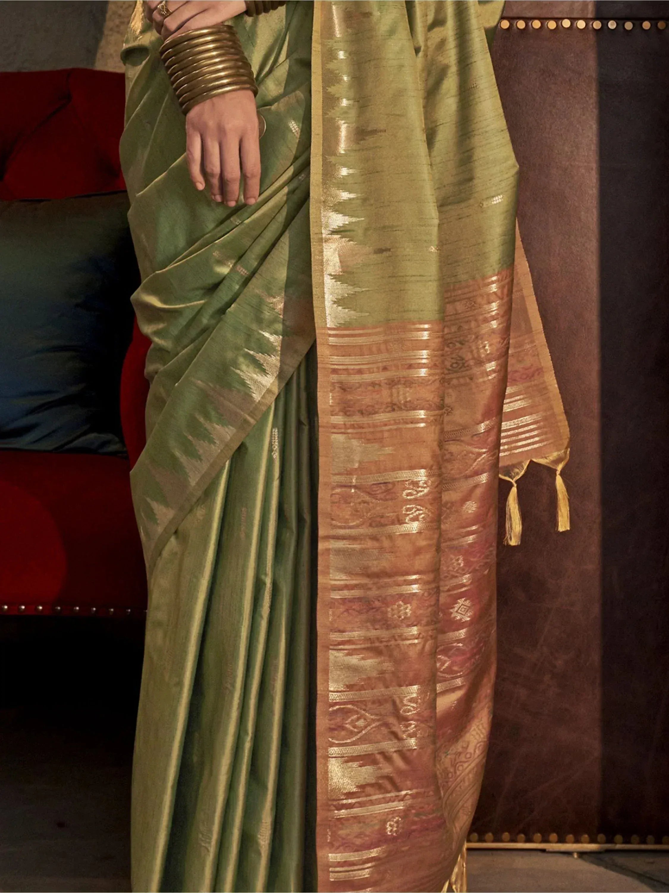 Olive green silk saree with gold zari border and intricate woven patterns, styled with traditional bangles