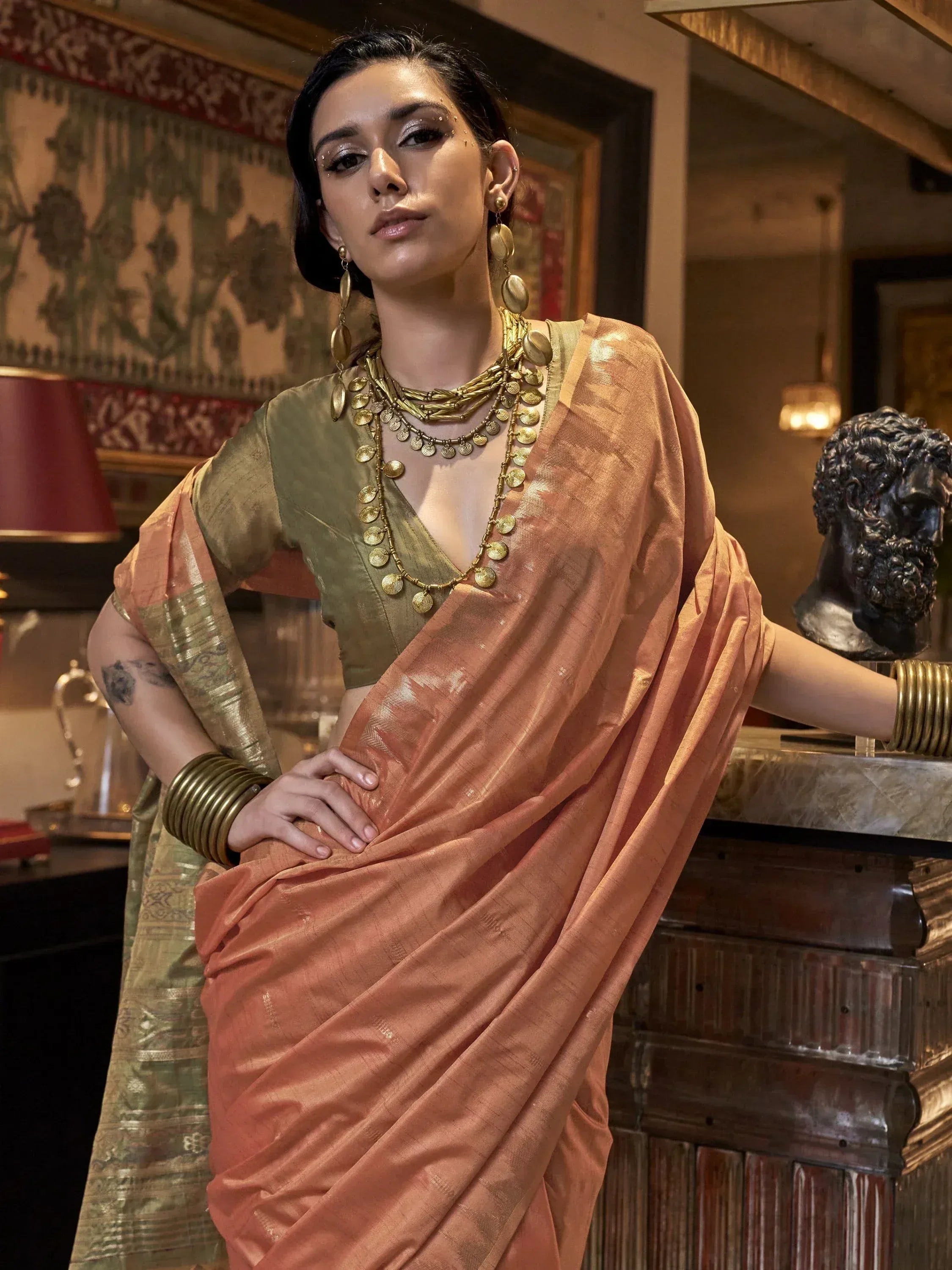 Woman in peach and olive green designer saree with gold jewelry, ethnic Indian wear