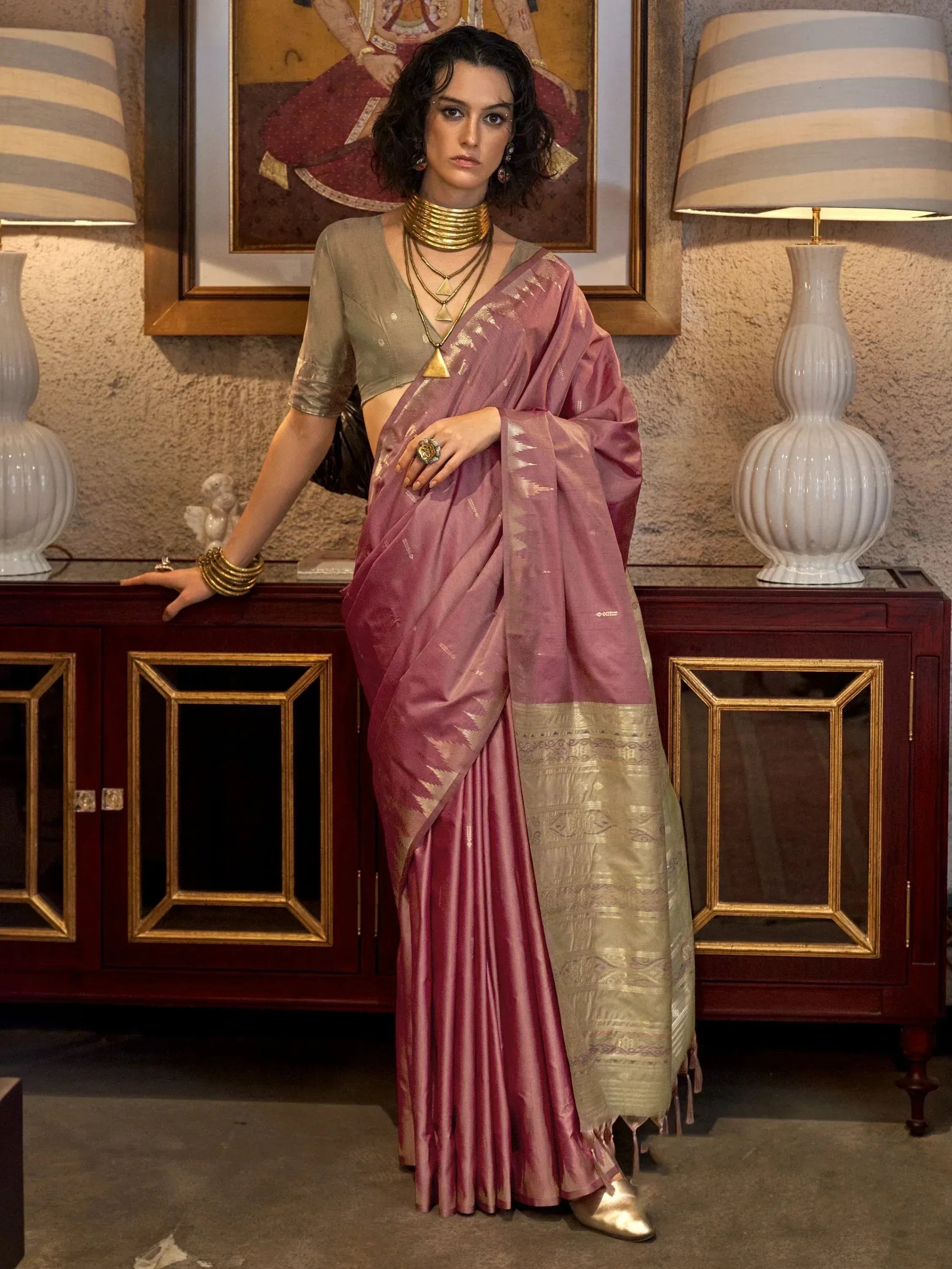 Woman in elegant mauve silk saree with gold border, paired with olive blouse and statement gold jewelry.