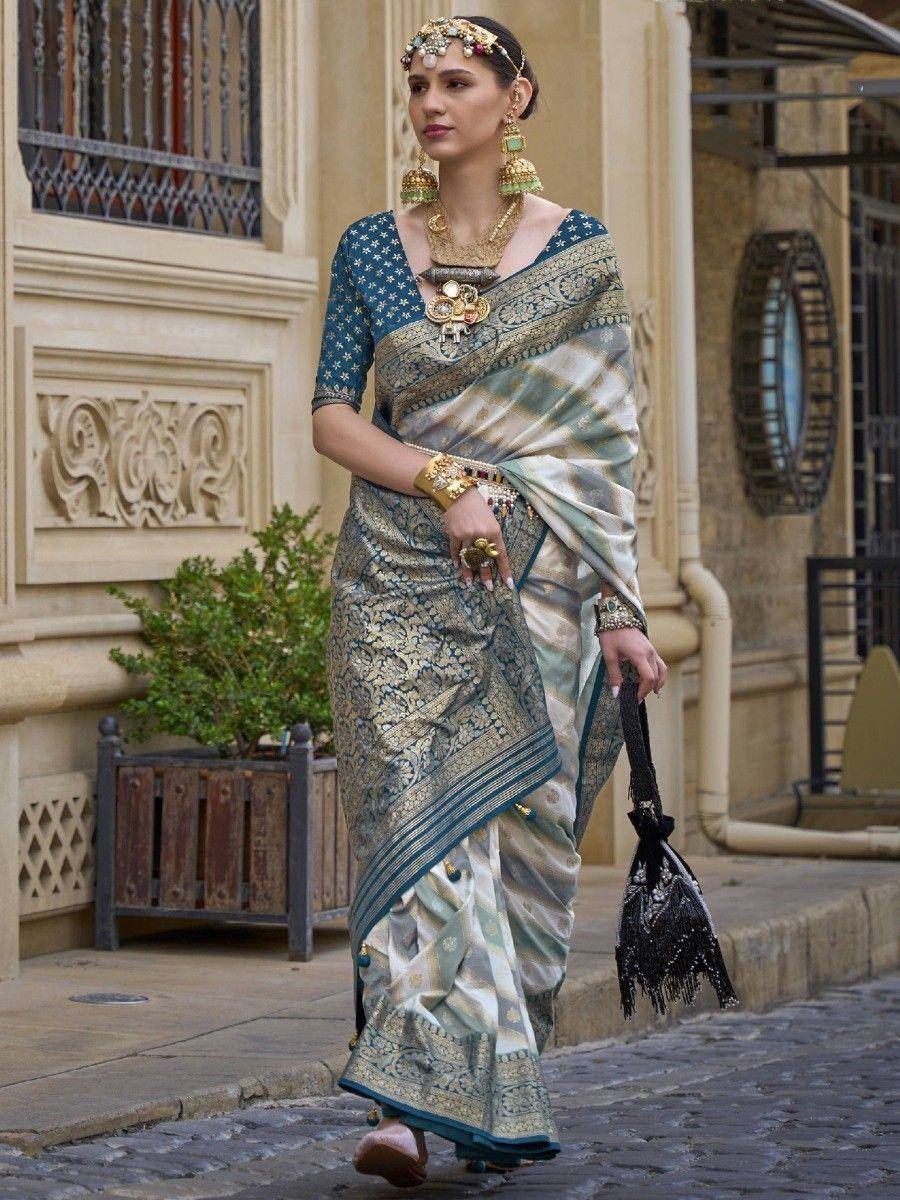 Elegant woman in designer saree with gold embroidery, traditional jewelry, and blue blouse, walking outdoors